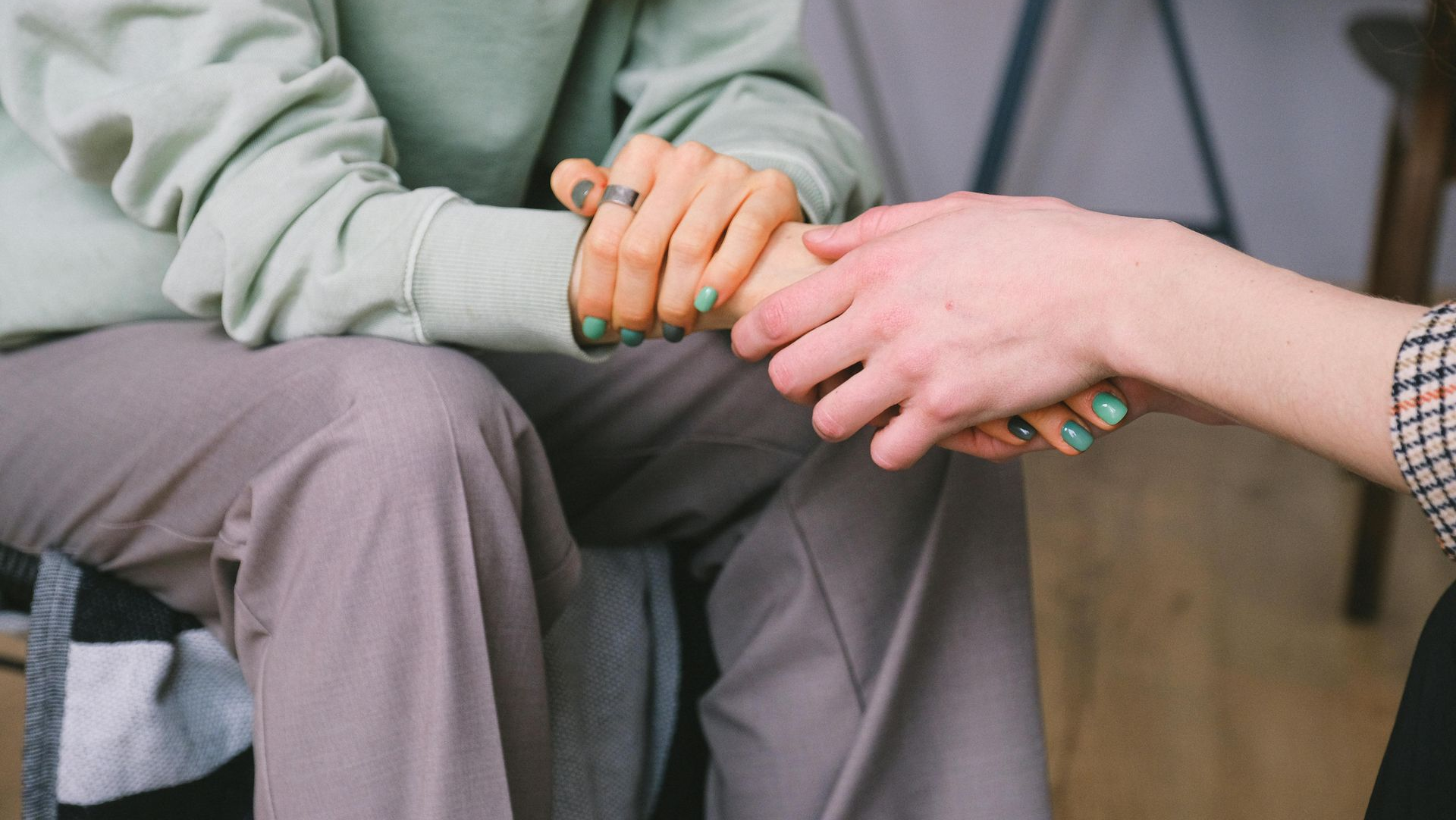 Two people holding hands, person in gray sweatshirt offering comfort, indoors.