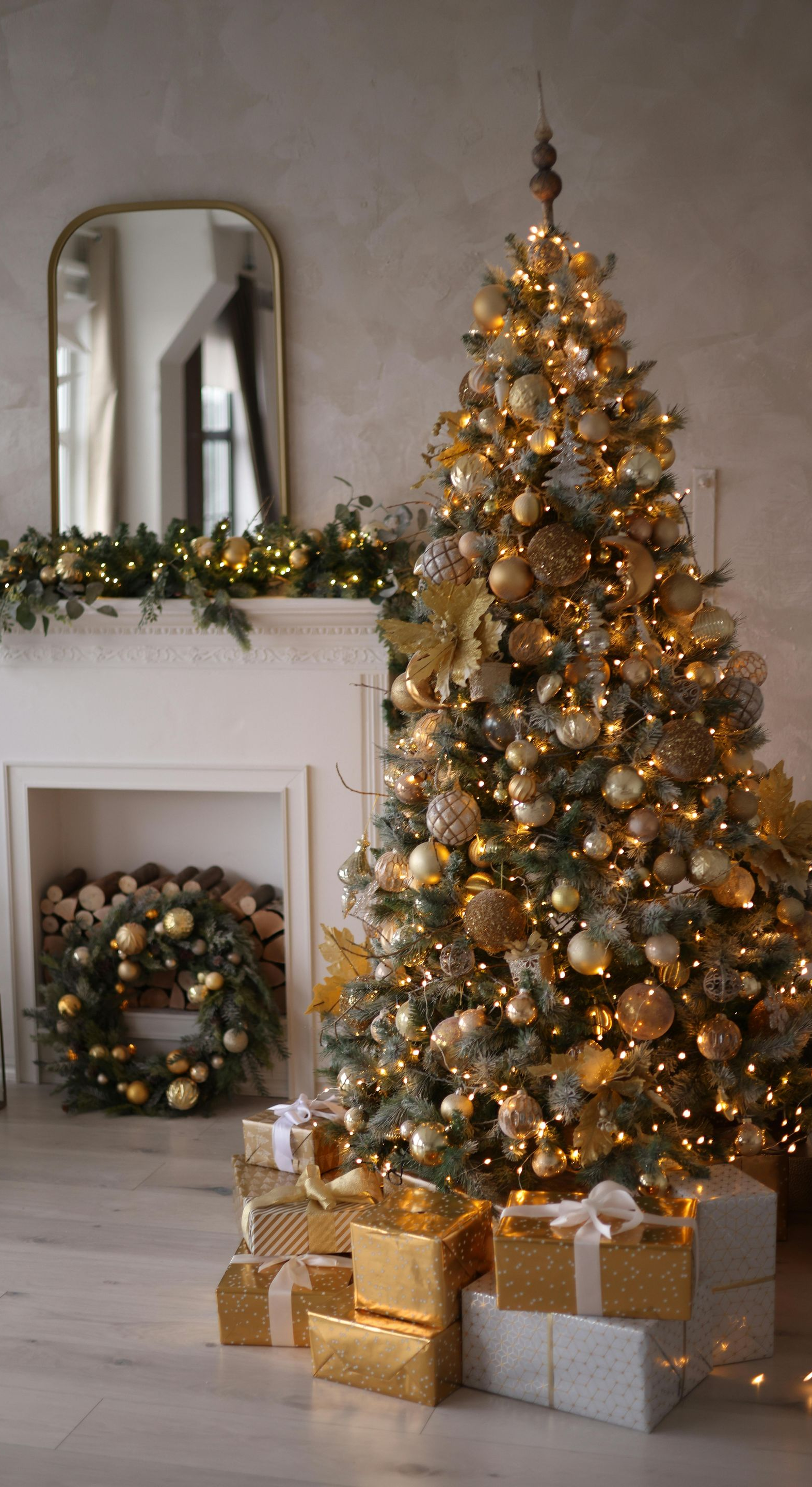 Christmas tree and gifts by a fireplace, adorned with gold ornaments and lights.
