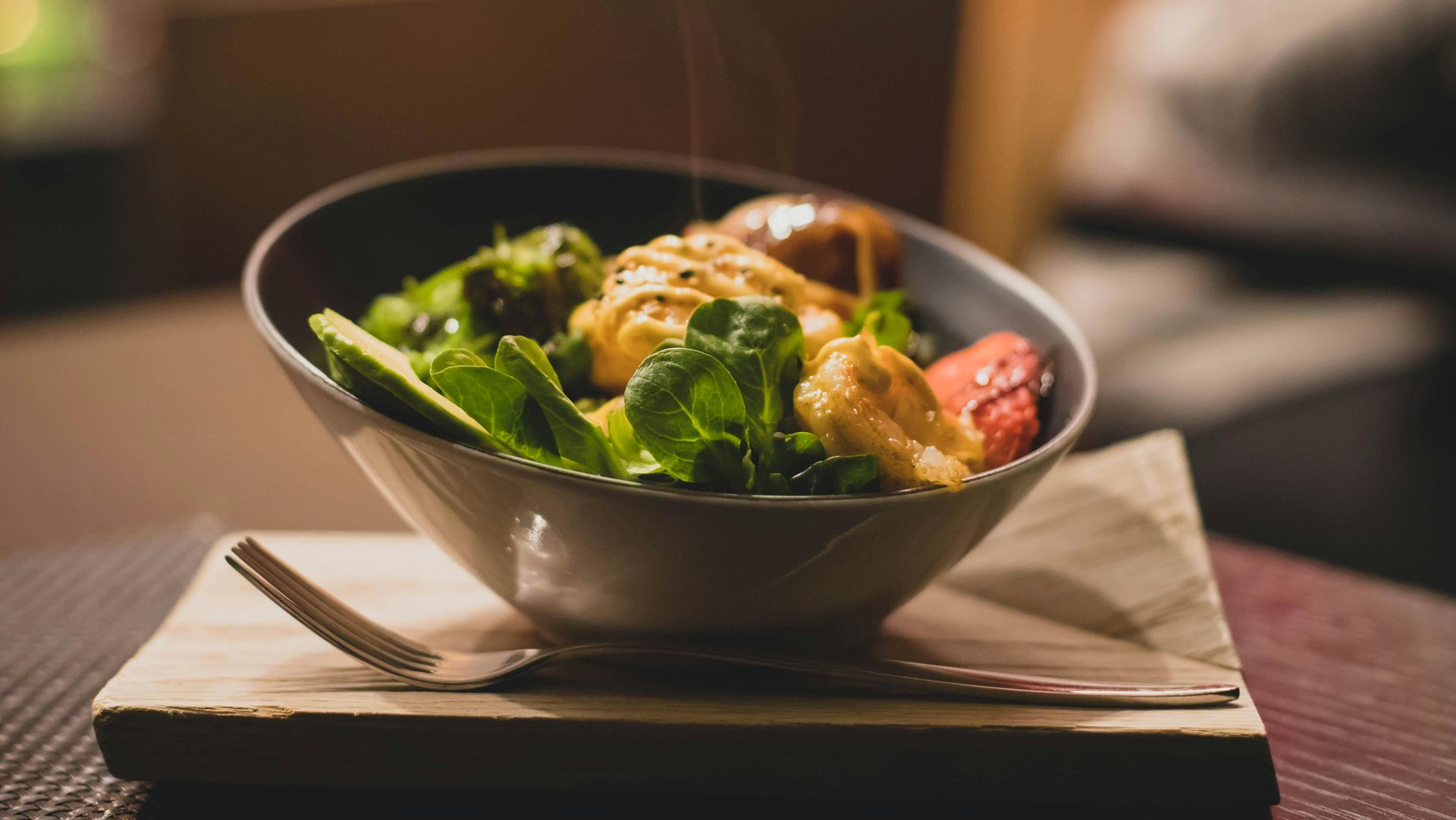 Salad in a bowl on a wooden board with a fork. Green vegetables, tofu, and sauce visible.