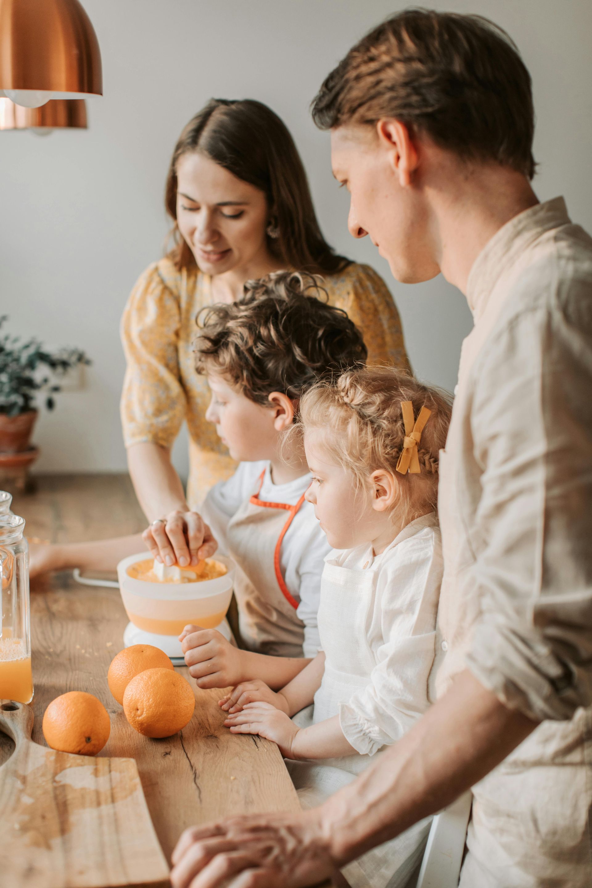 Family in kitchen squeezing oranges. Blonde mother, father, and two children.