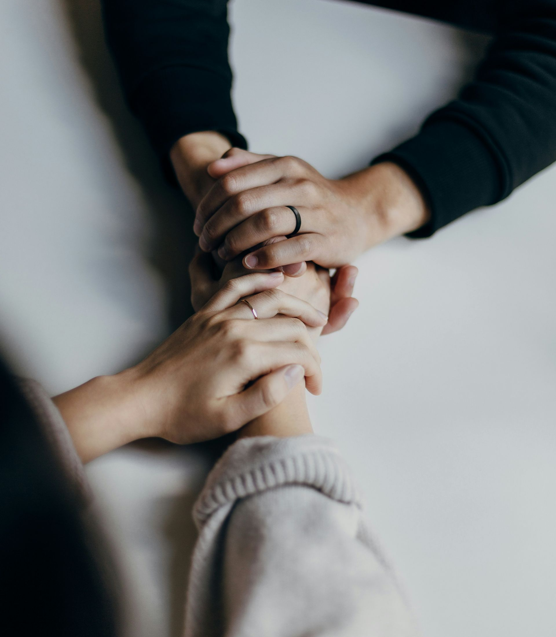Three sets of hands clasped together on a white surface, suggesting support or comfort.