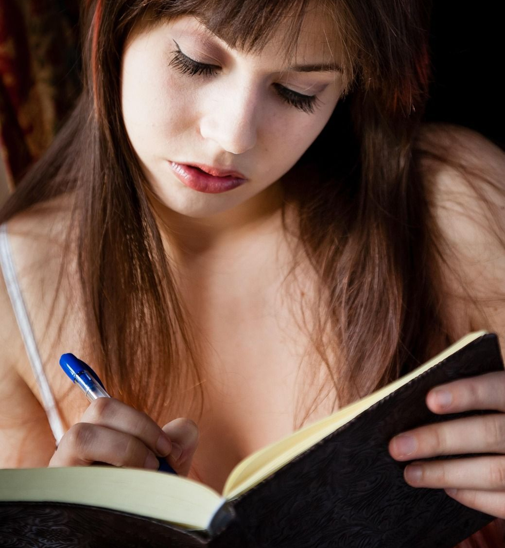 Young woman writes in a notebook with a pen, soft lighting.