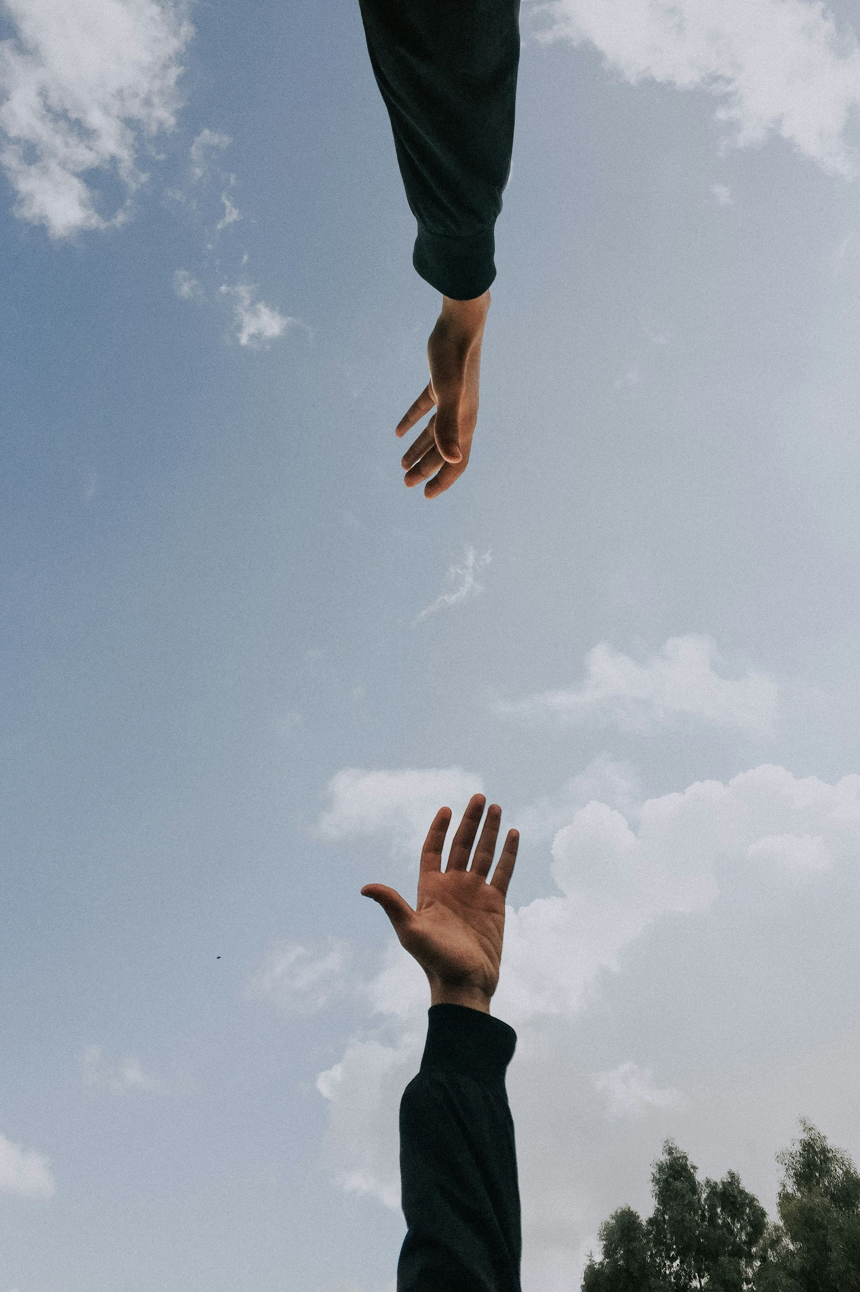 Two hands reaching toward each other against a cloudy sky.