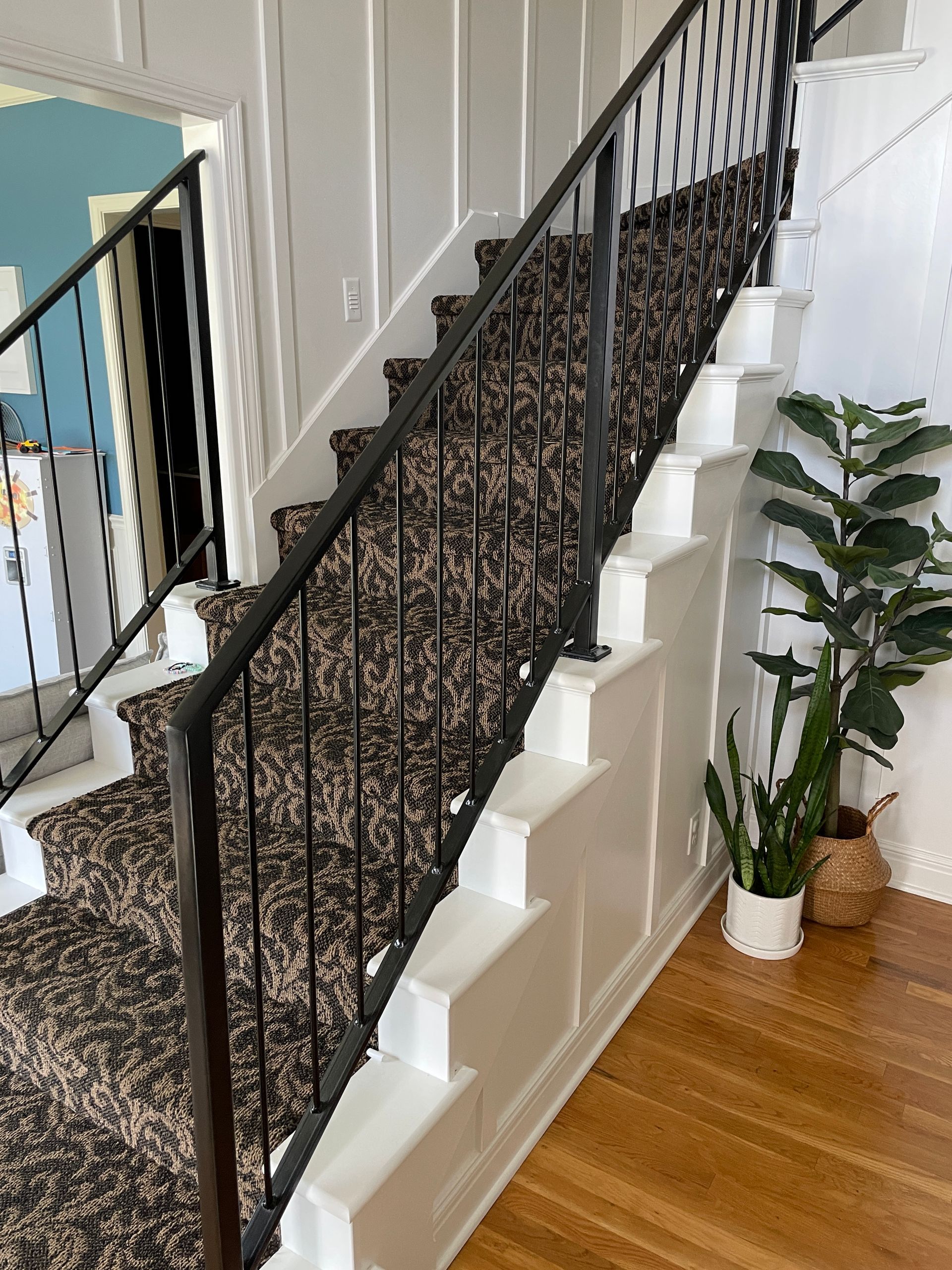 A staircase with a black railing and a plant in the corner.