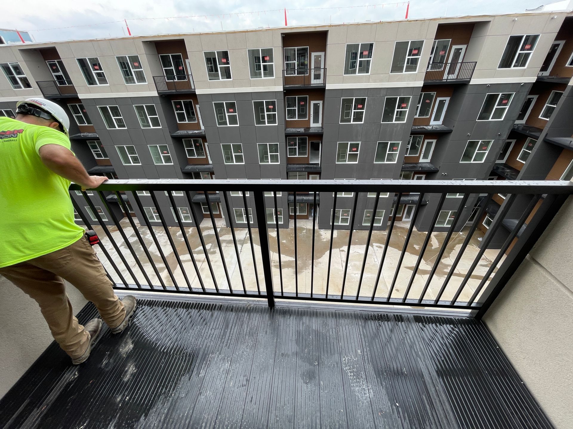 A man is installing a handrail on a balcony overlooking a building.