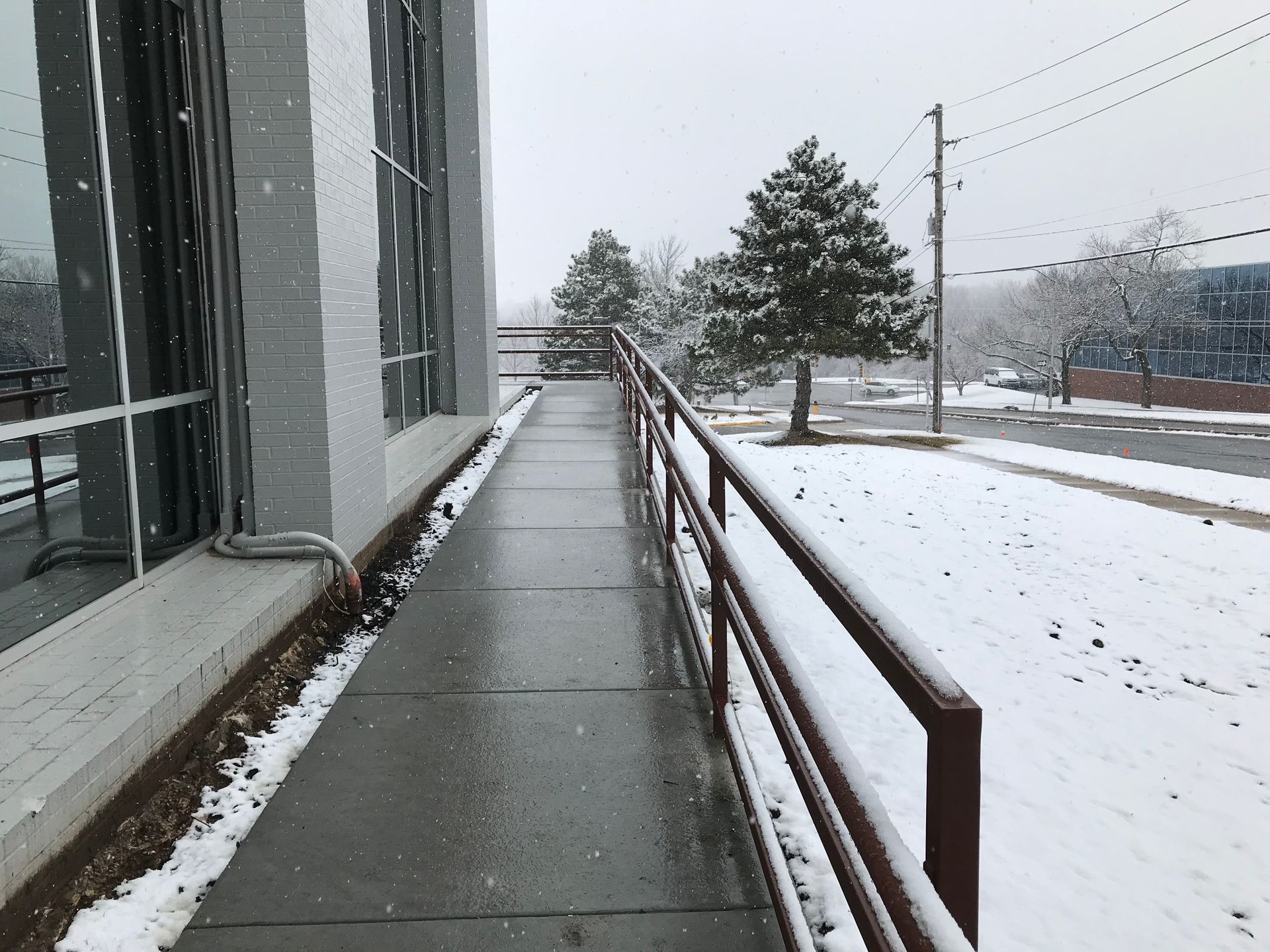 A snowy sidewalk with a railing and a building in the background