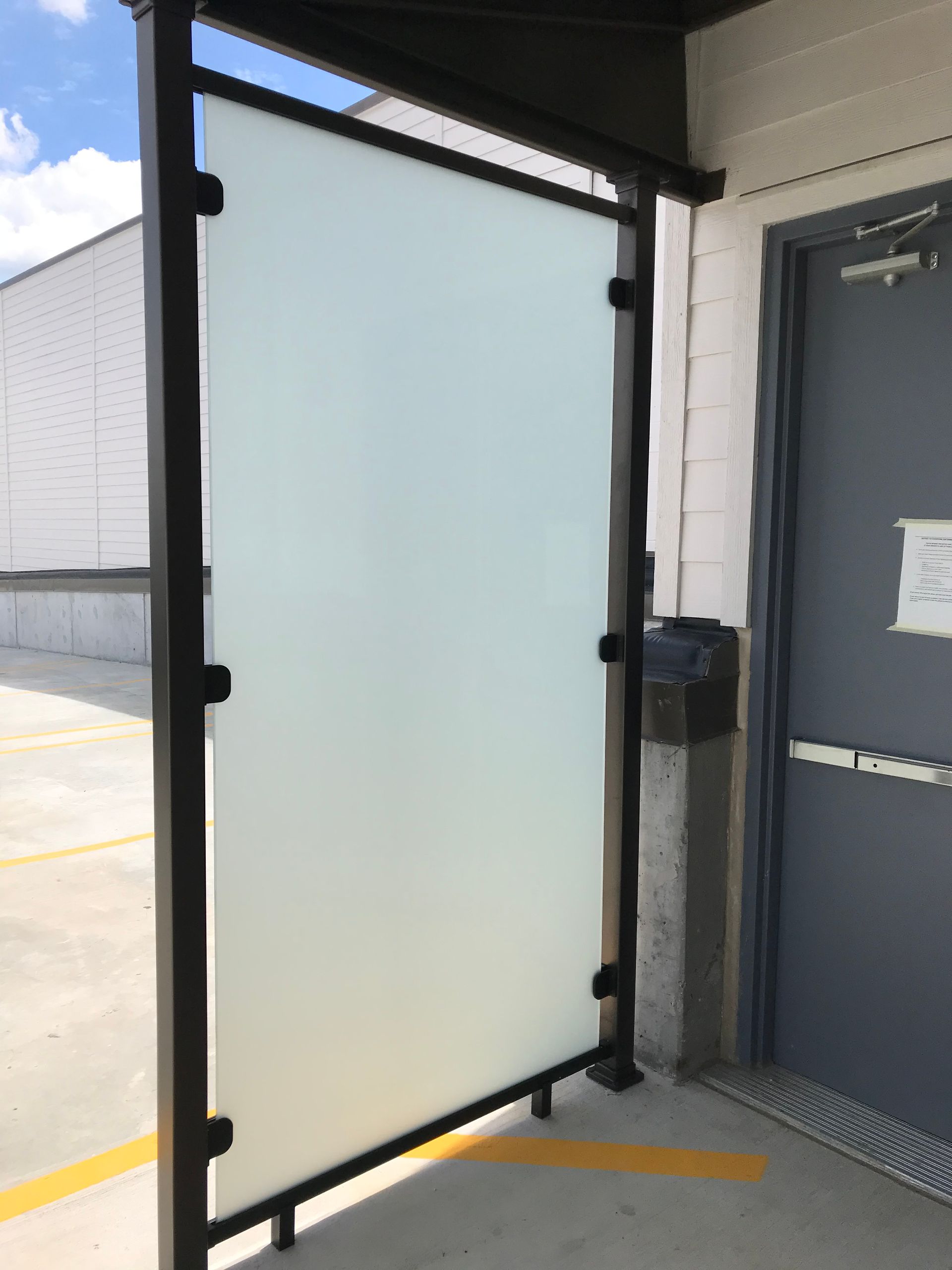 A black aluminum privacy fence with glass is sitting next to a door in a parking lot.