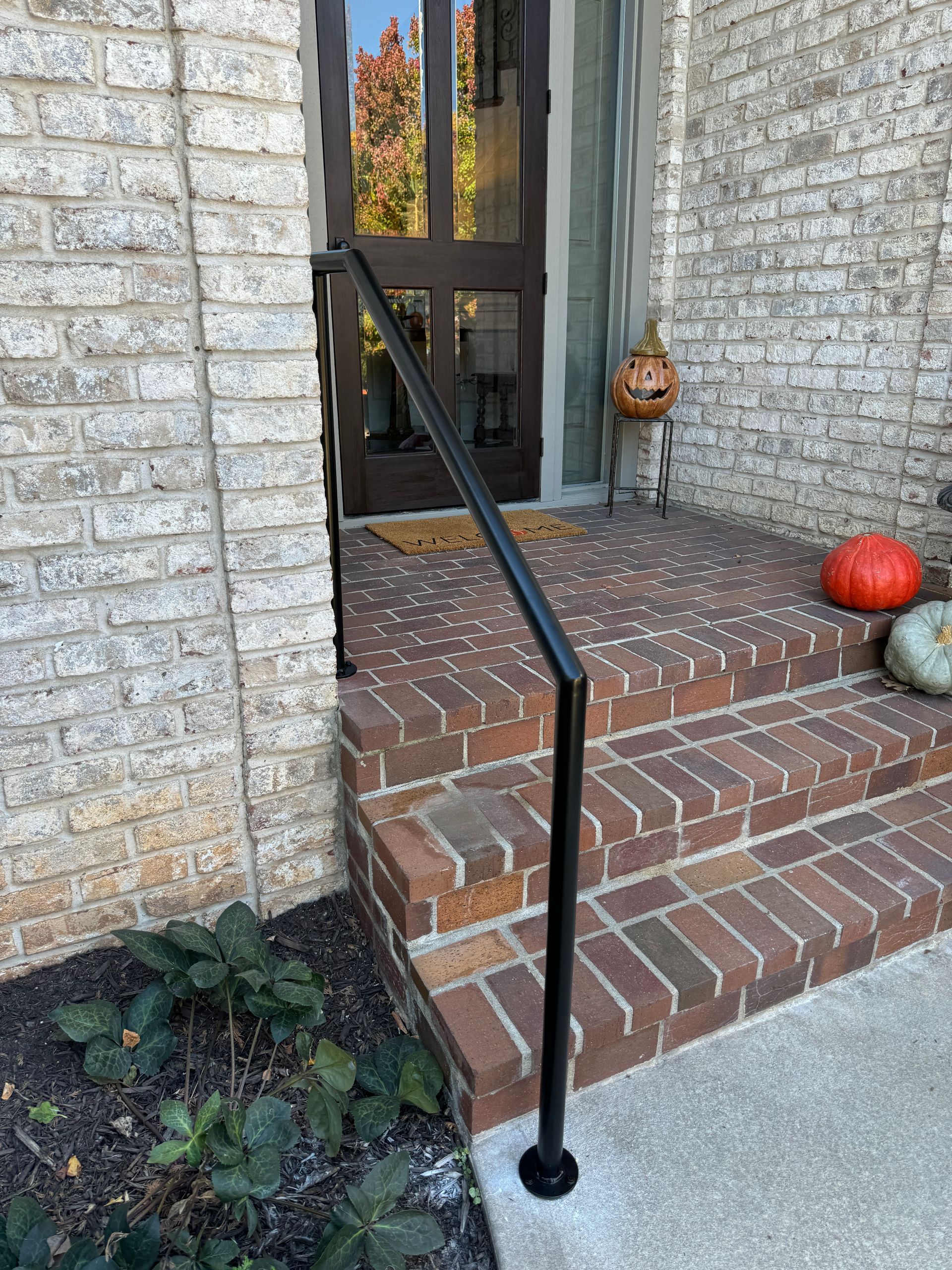 There is a black railing on the porch of a brick house.