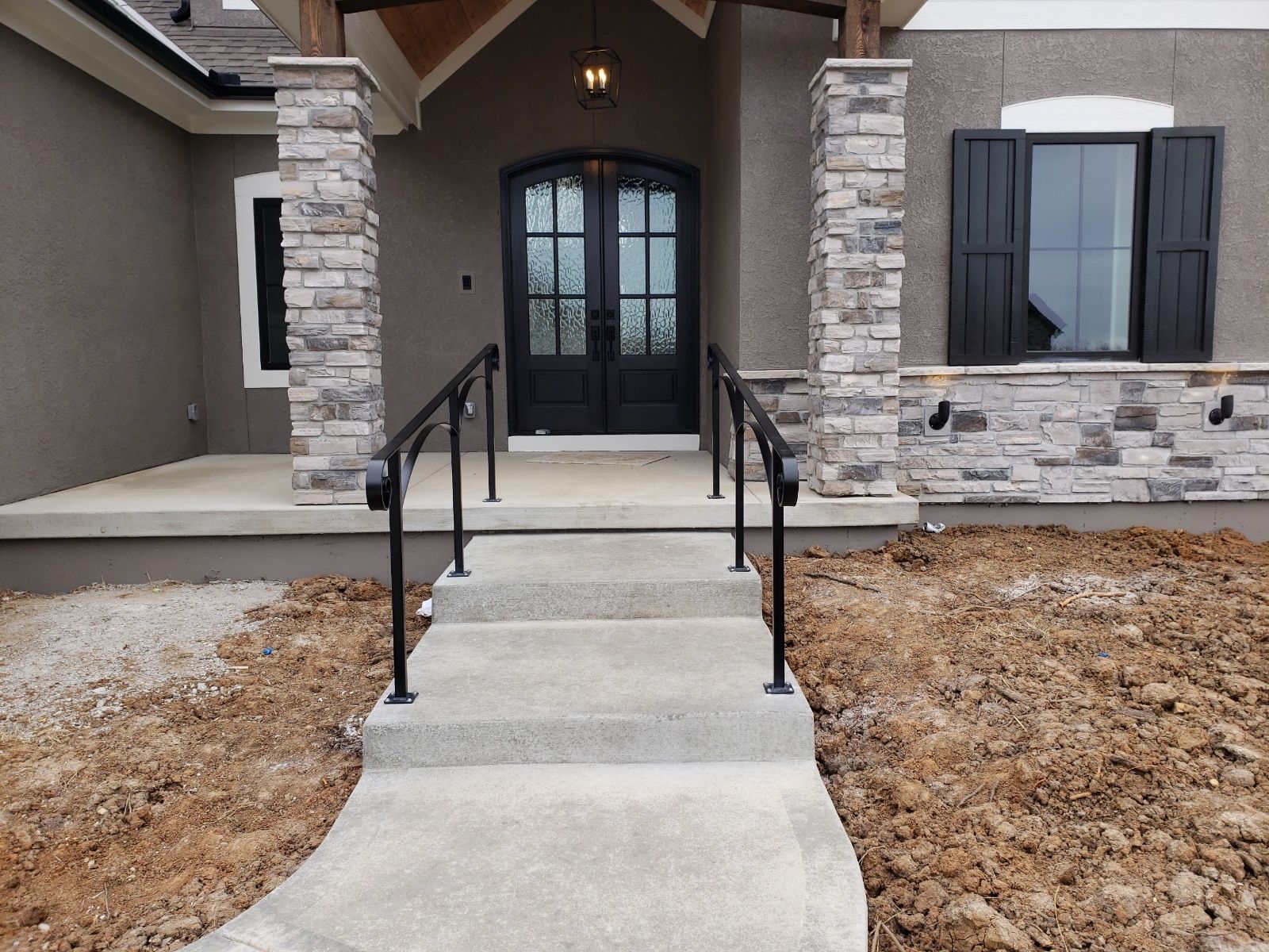 A concrete walkway leads to the front door of a house with black railing