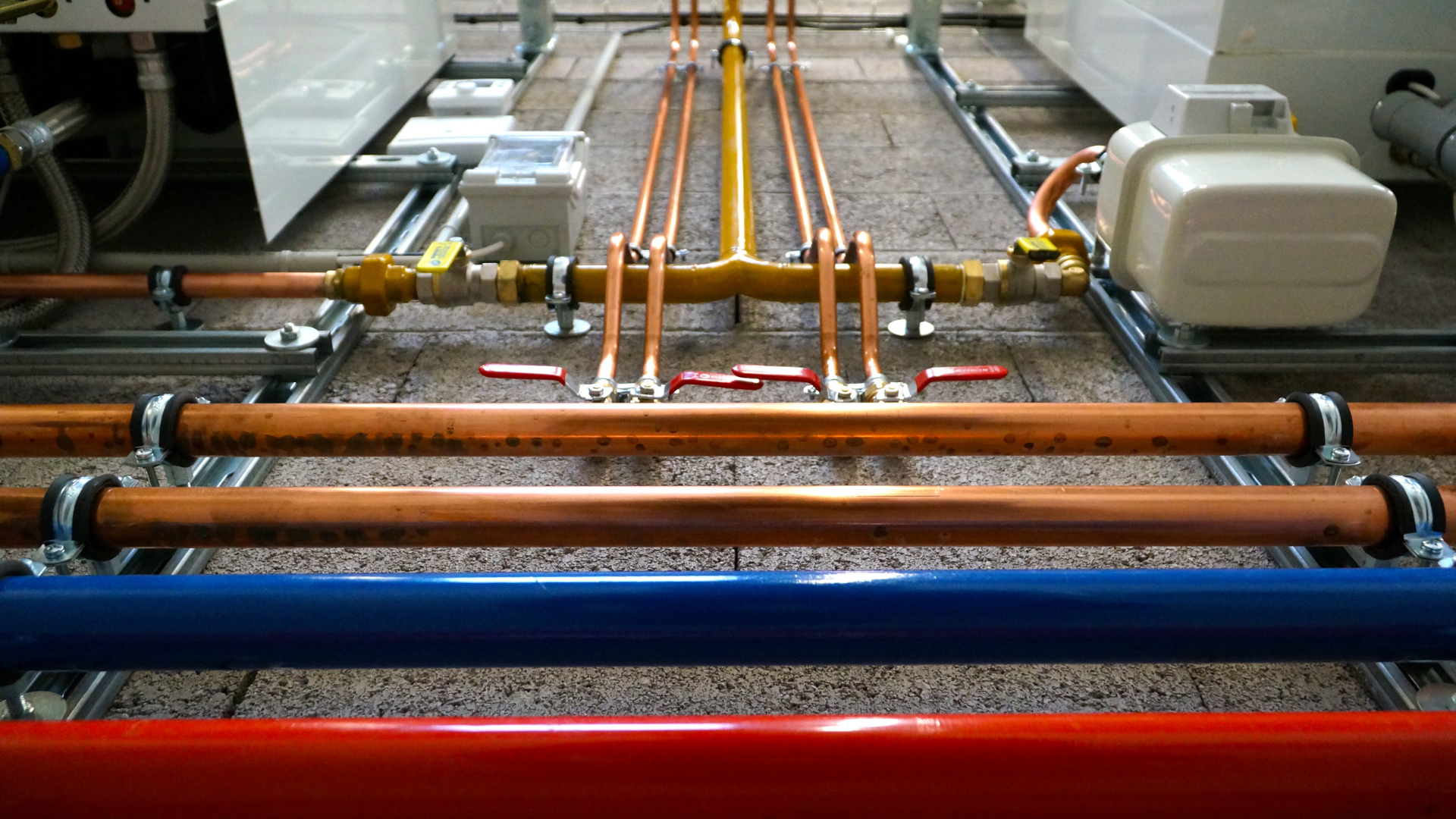 Copper, blue, and red pipes secured on metal supports, part of an industrial plumbing system.