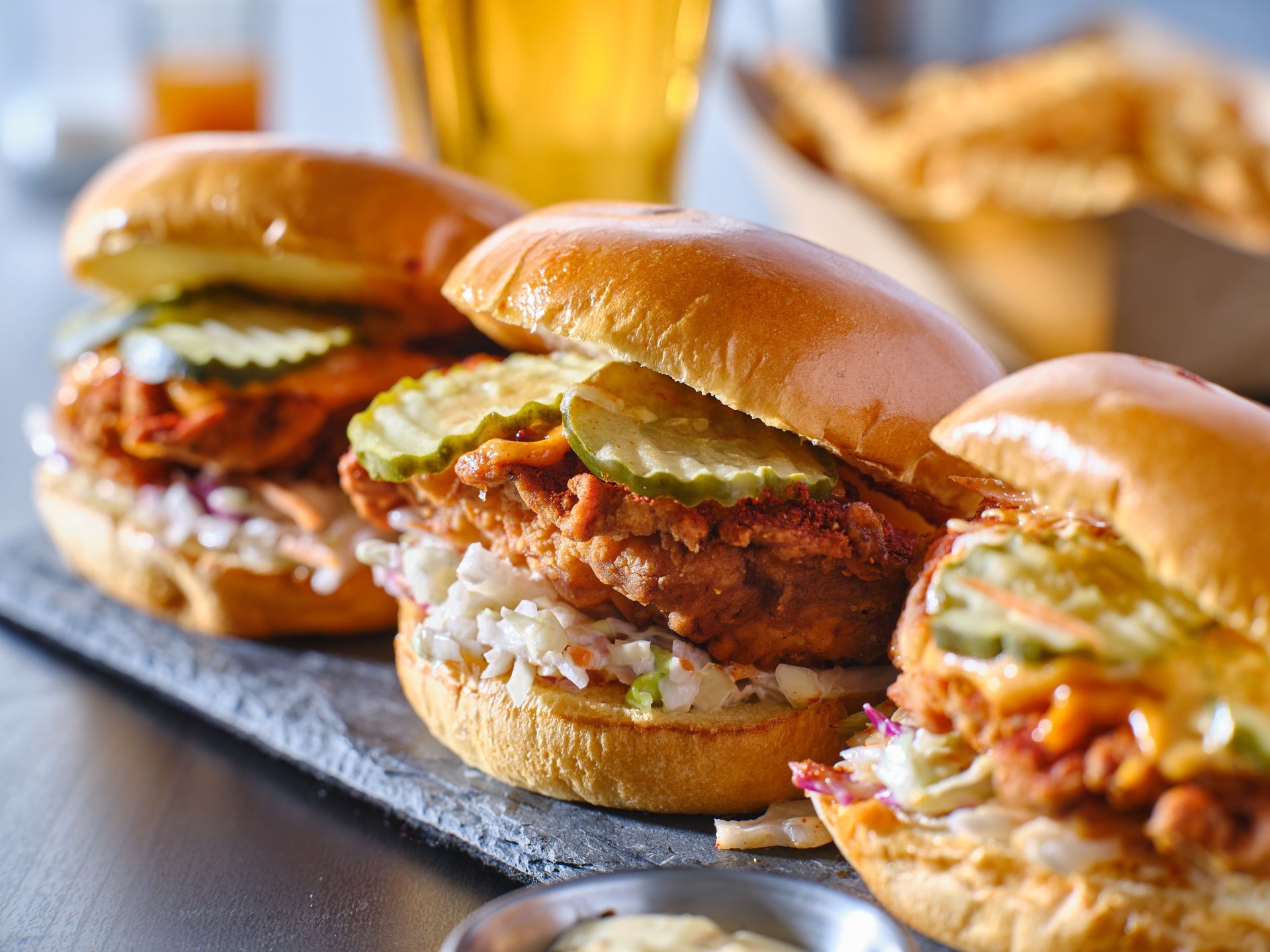 Three chicken sandwiches are sitting on a slate tray on a table.