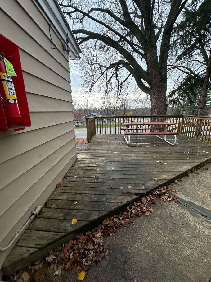 A wooden deck with a picnic table and a fire extinguisher on the side of a building.