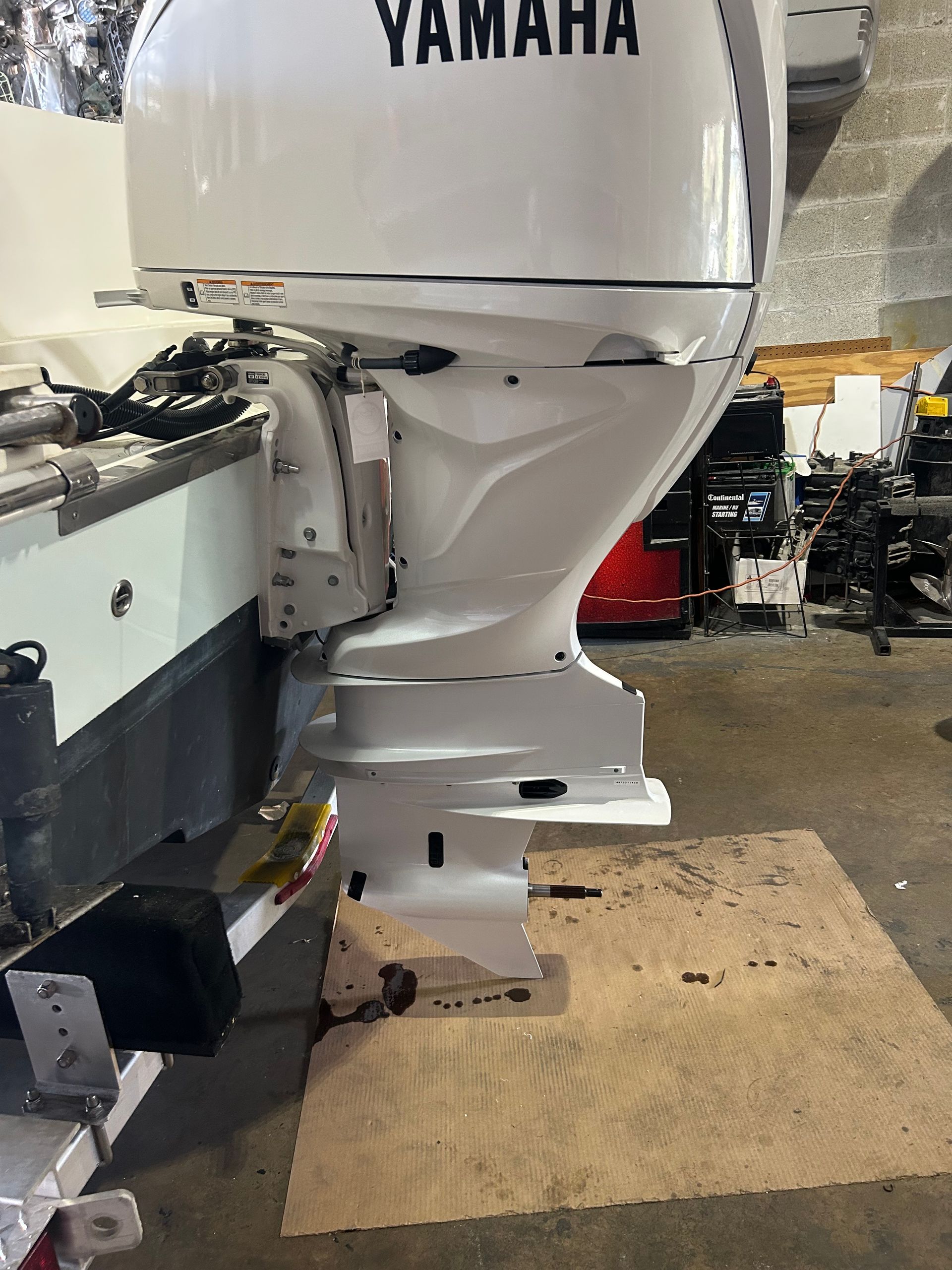 White Yamaha outboard motor attached to a boat, in a workshop setting.