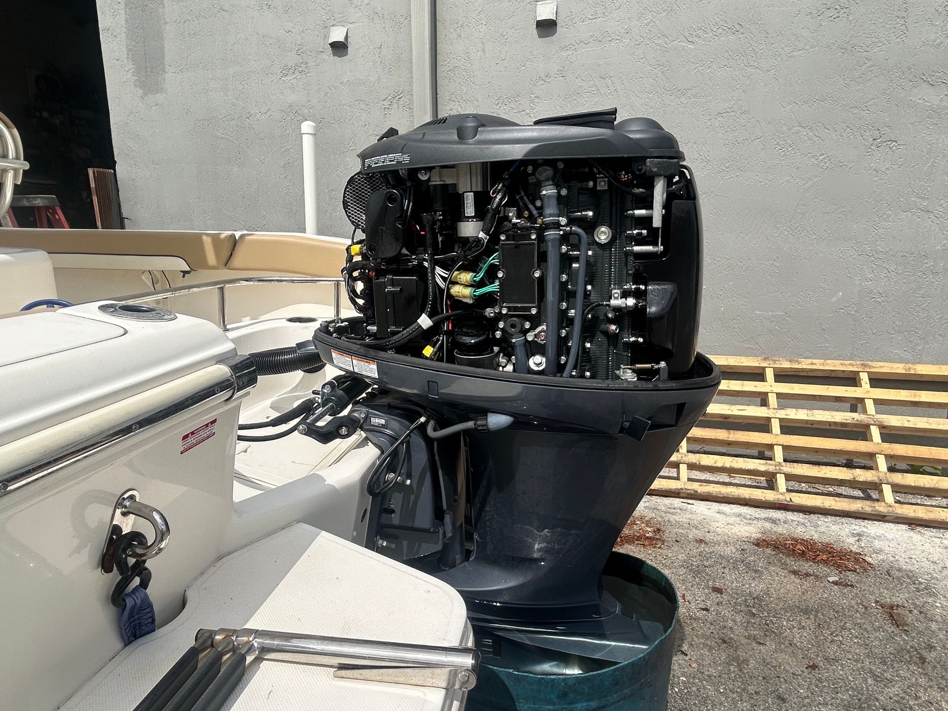 Black outboard motor mounted on a boat, outside against a gray wall.