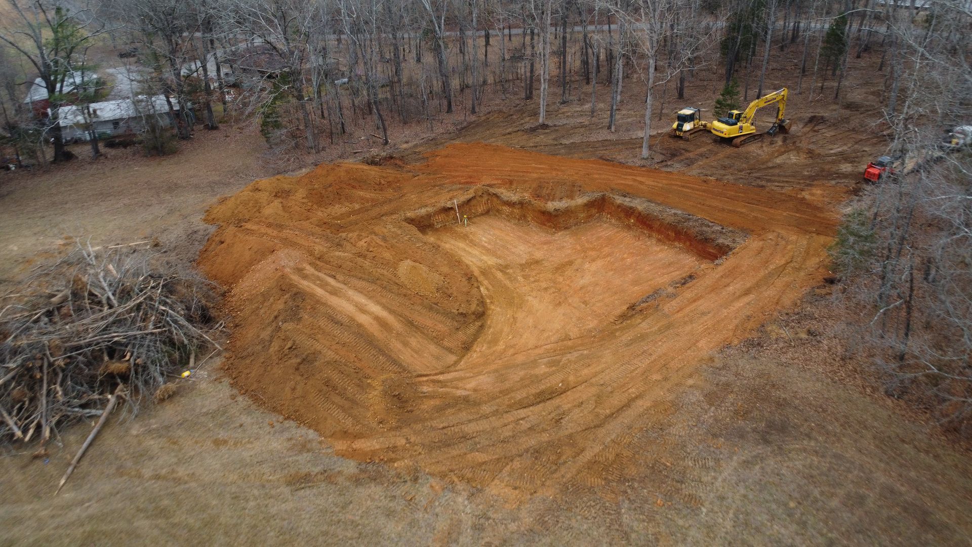 A view from inside an excavator cab looking out at a field of dirt and brush with the machine's metal claw visible.