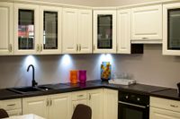 White kitchen cabinets with black countertops and sink; under-cabinet lighting.