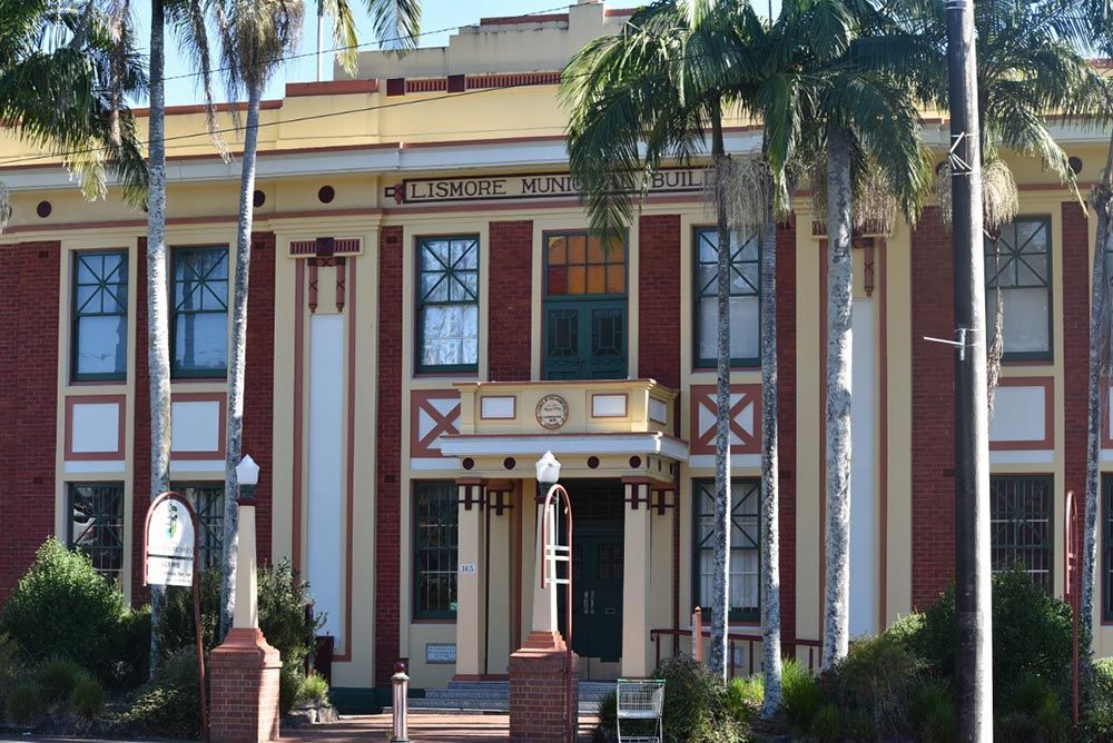 A Brick Building With Palm Trees In Front Of It — All Roof Restorations & Solar In Lismore, NSW