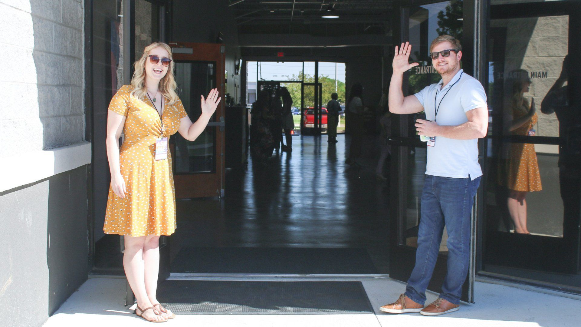 A man and a woman waving at the camera standing at open doors - Mosaic Church, Freeport, FL