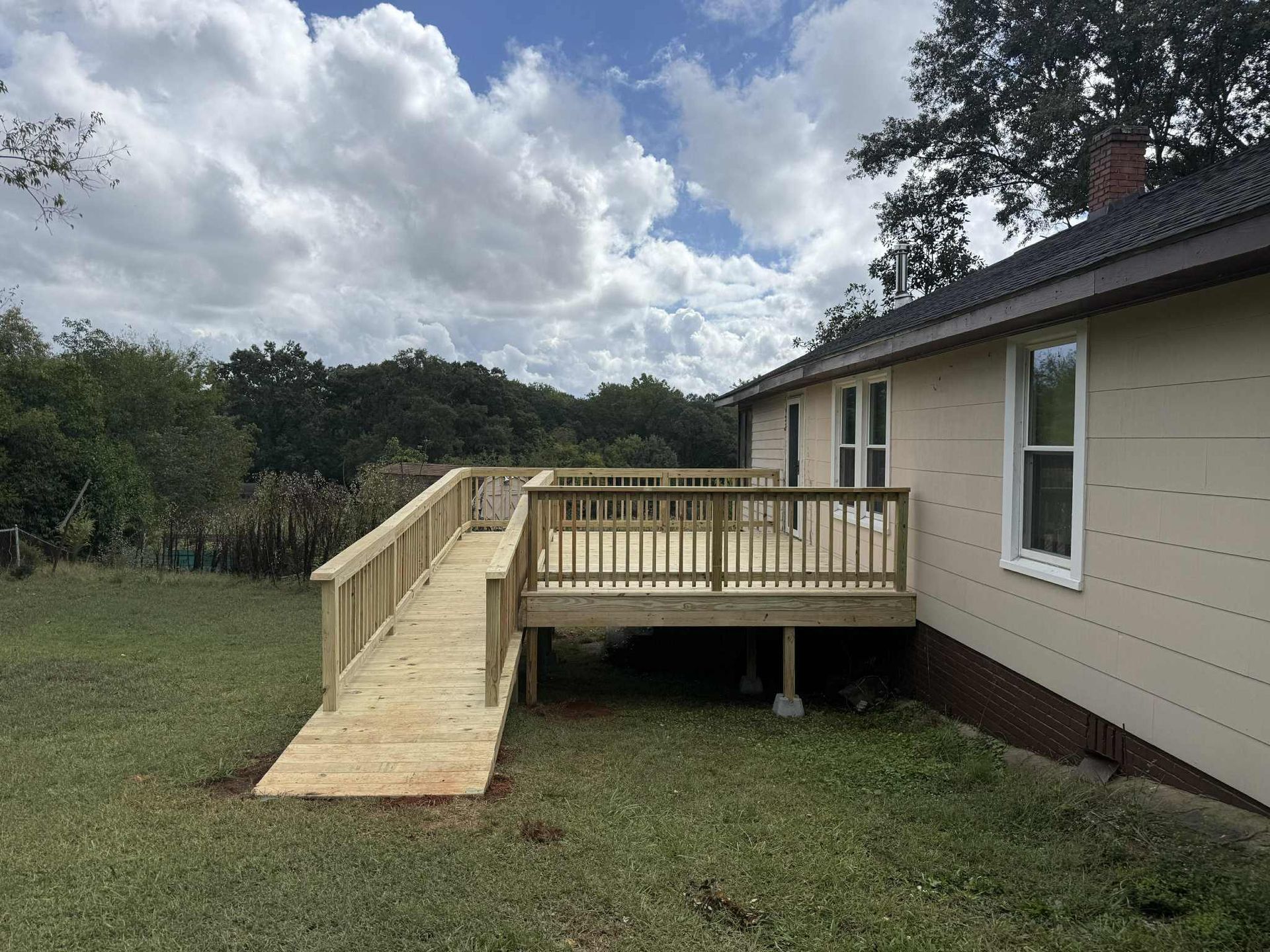 Wooden deck with ramp attached to a house with beige siding, set on a grassy lawn.