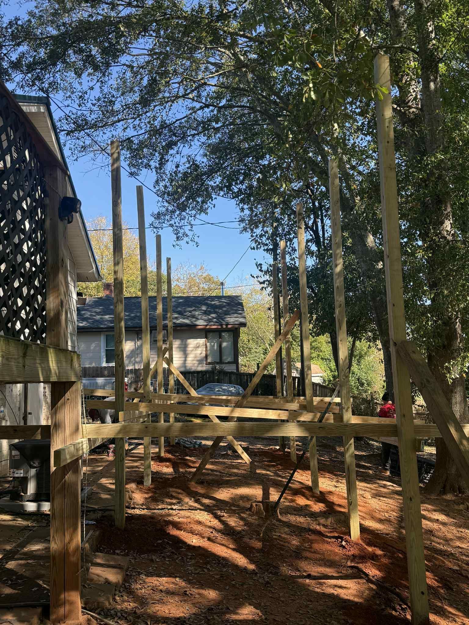Wooden framework under construction in a yard, with vertical support posts and overhead beams.