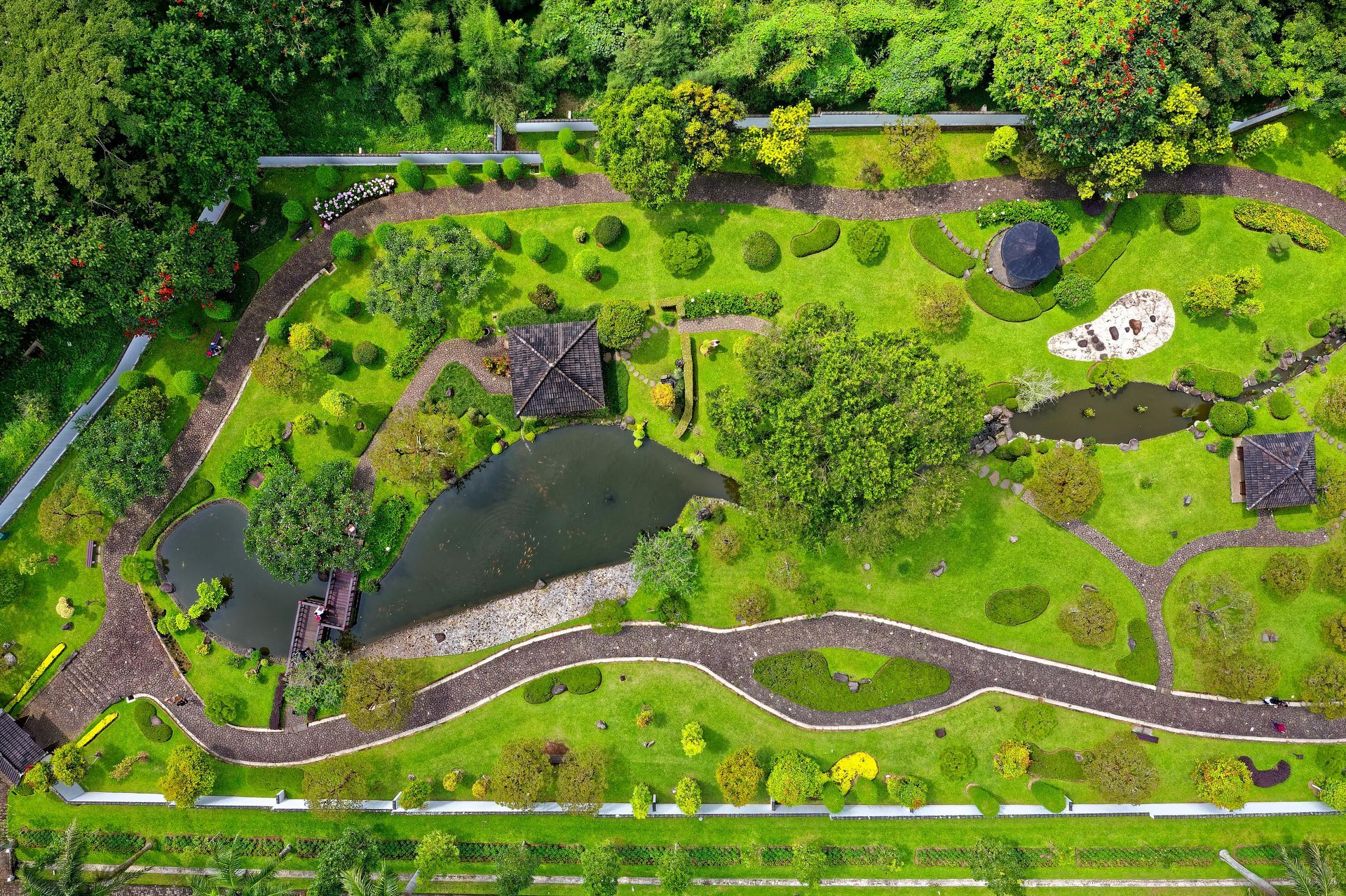 Aerial view of a lush green garden with winding pathways, ponds, and varied vegetation.