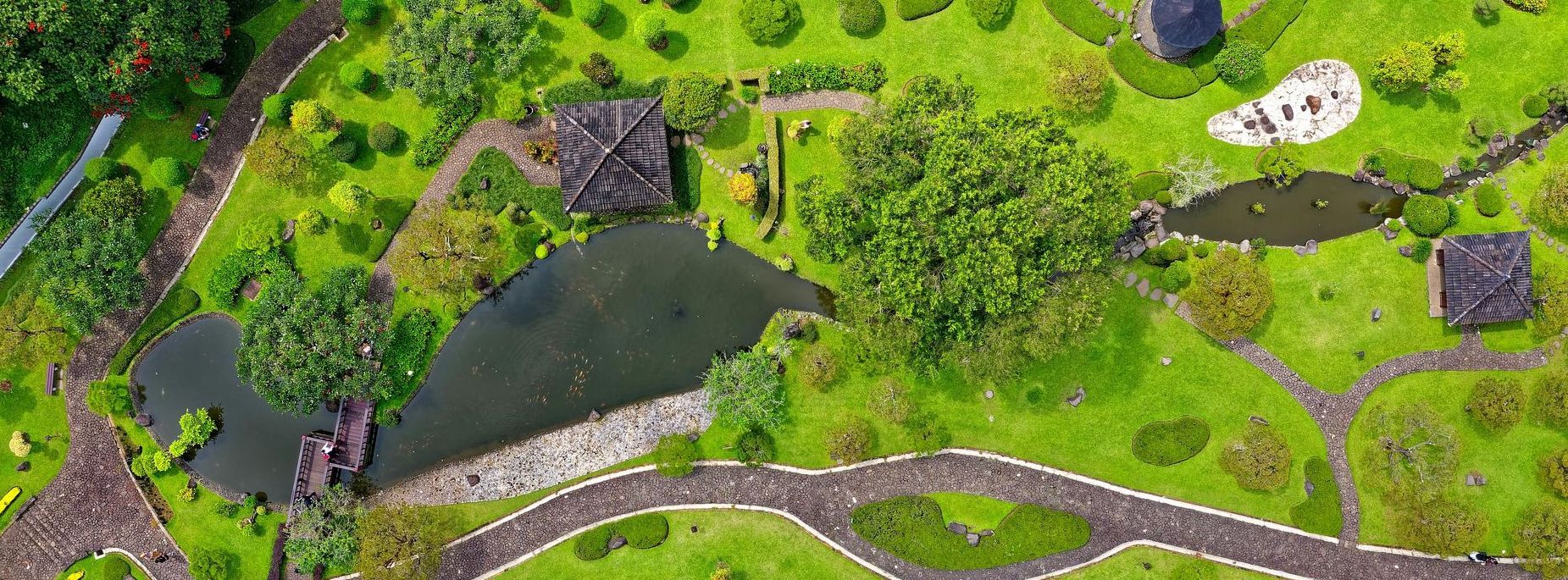Aerial view of a garden with ponds, stone paths, green lawns, and small buildings.