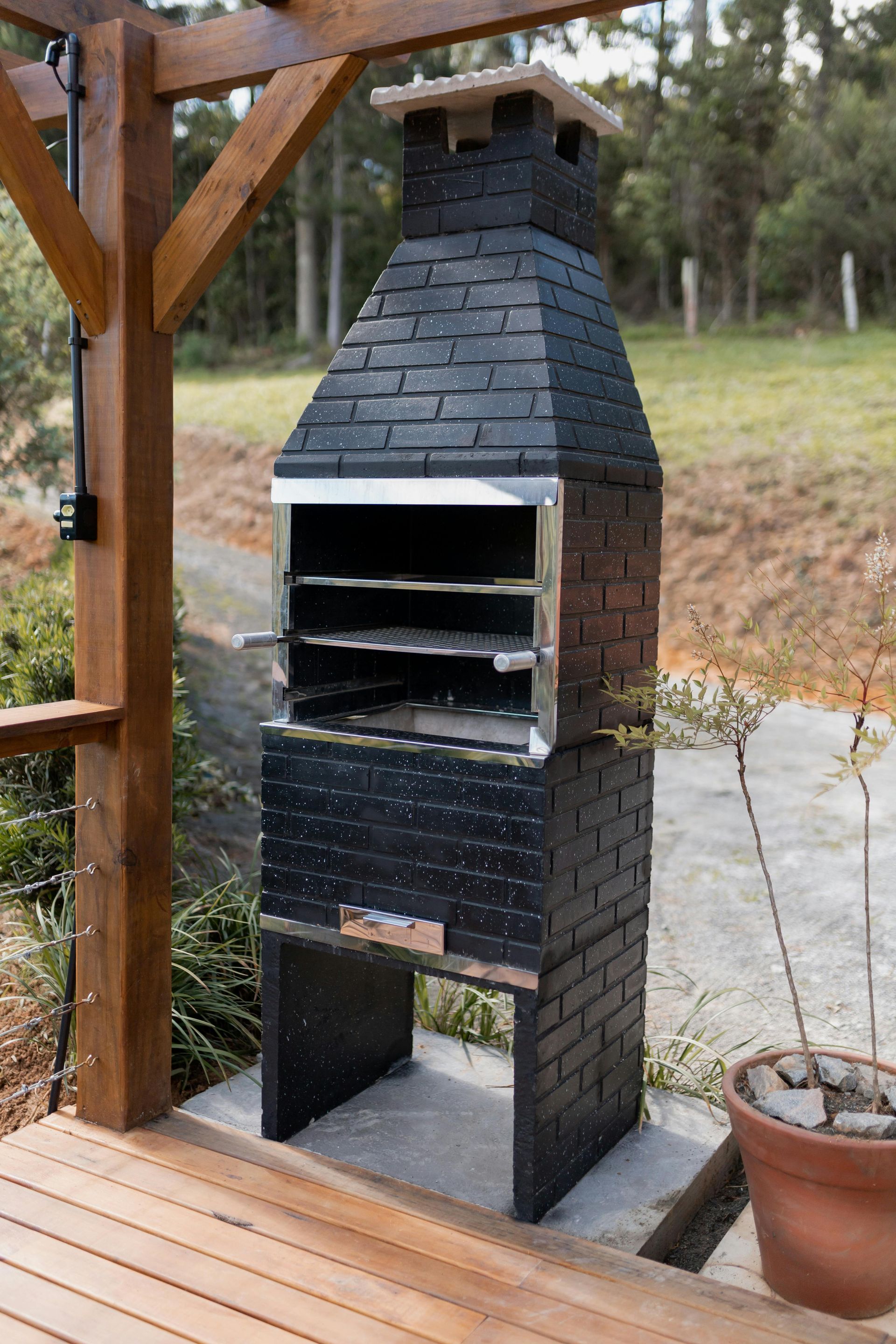 Outdoor brick barbecue grill next to wooden post on a patio.