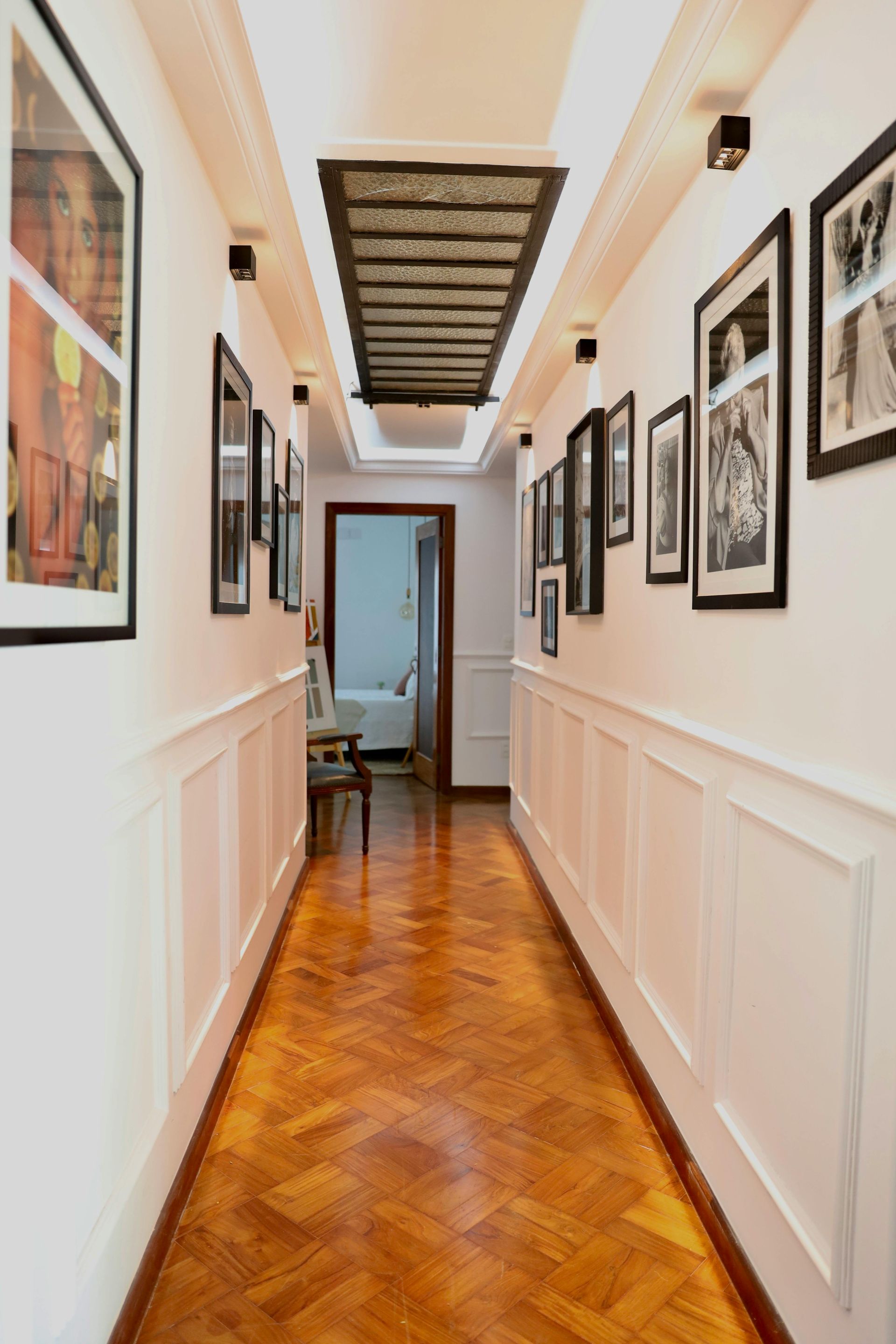 Long hallway with wood floor, white paneled walls, and framed photos.