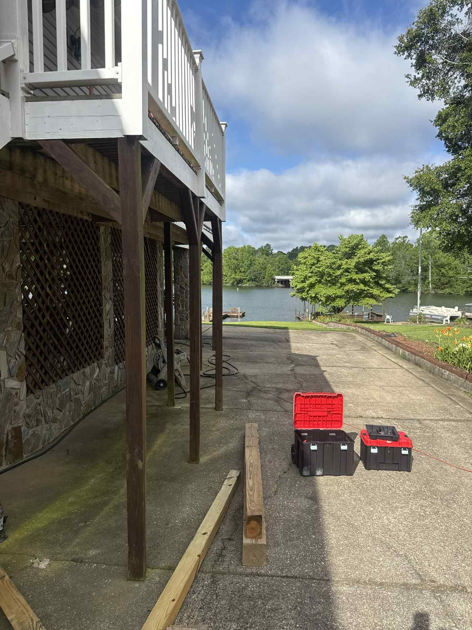 Deck with railing and supports, tool boxes on a concrete patio, overlooking a lake.