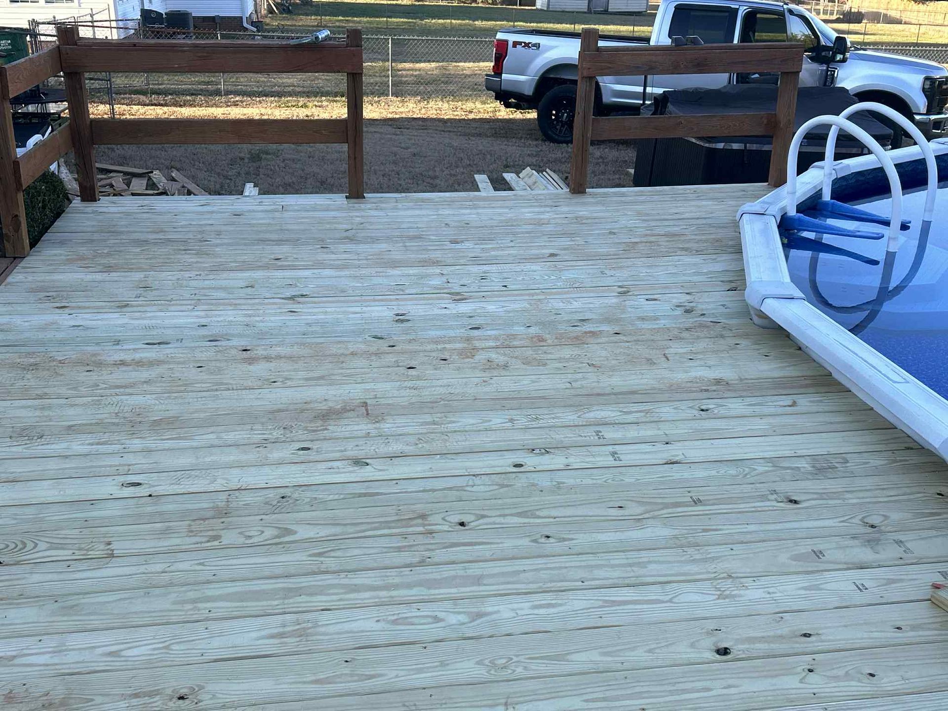 Wooden deck next to an above-ground pool; brown railings surround the deck. A truck is visible in the background.