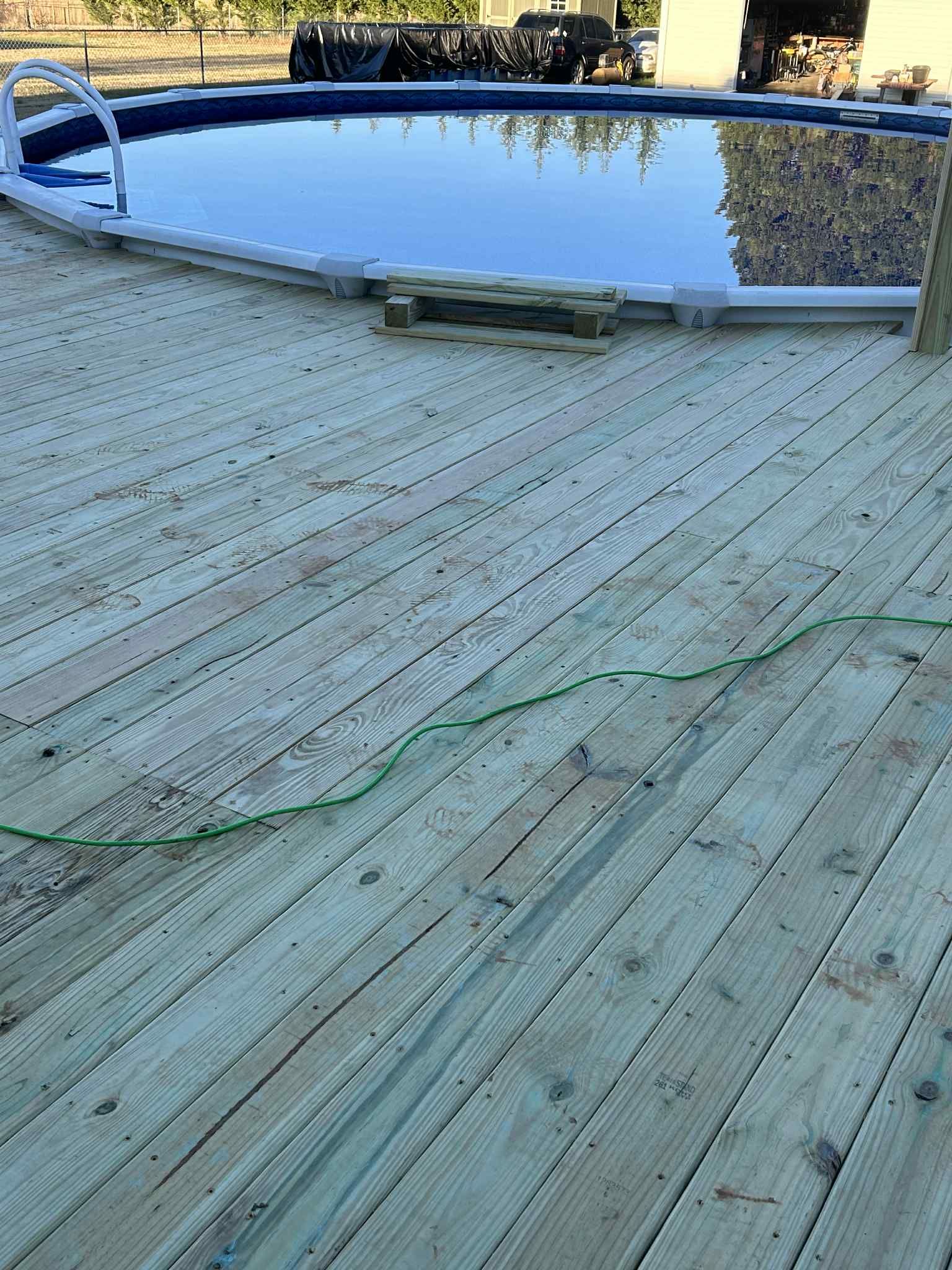 Wooden deck surrounding an above-ground pool. Green hose lies across the deck.