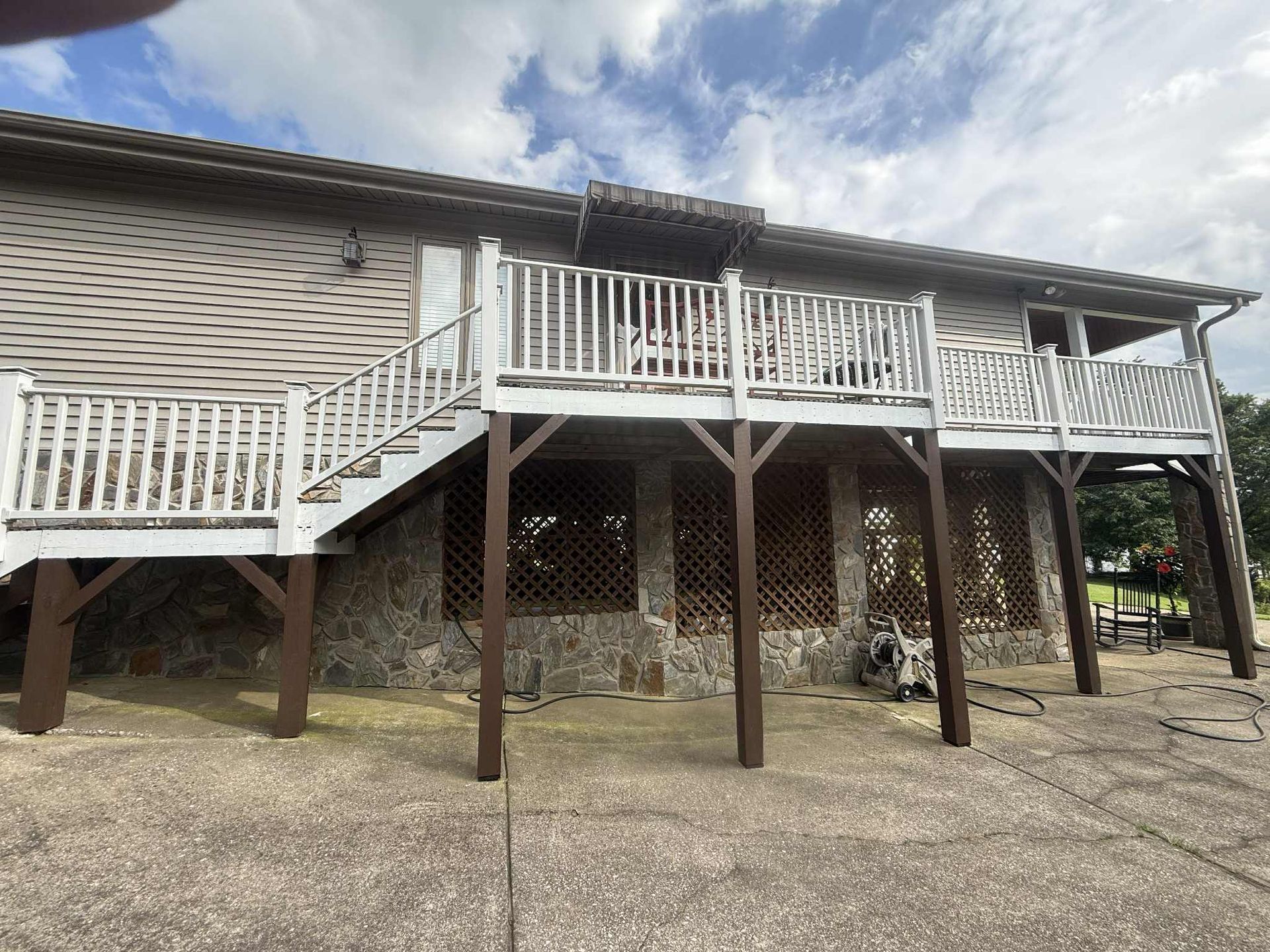 Exterior of a house with a wooden deck and stairs, brown support beams, and a stone facade.
