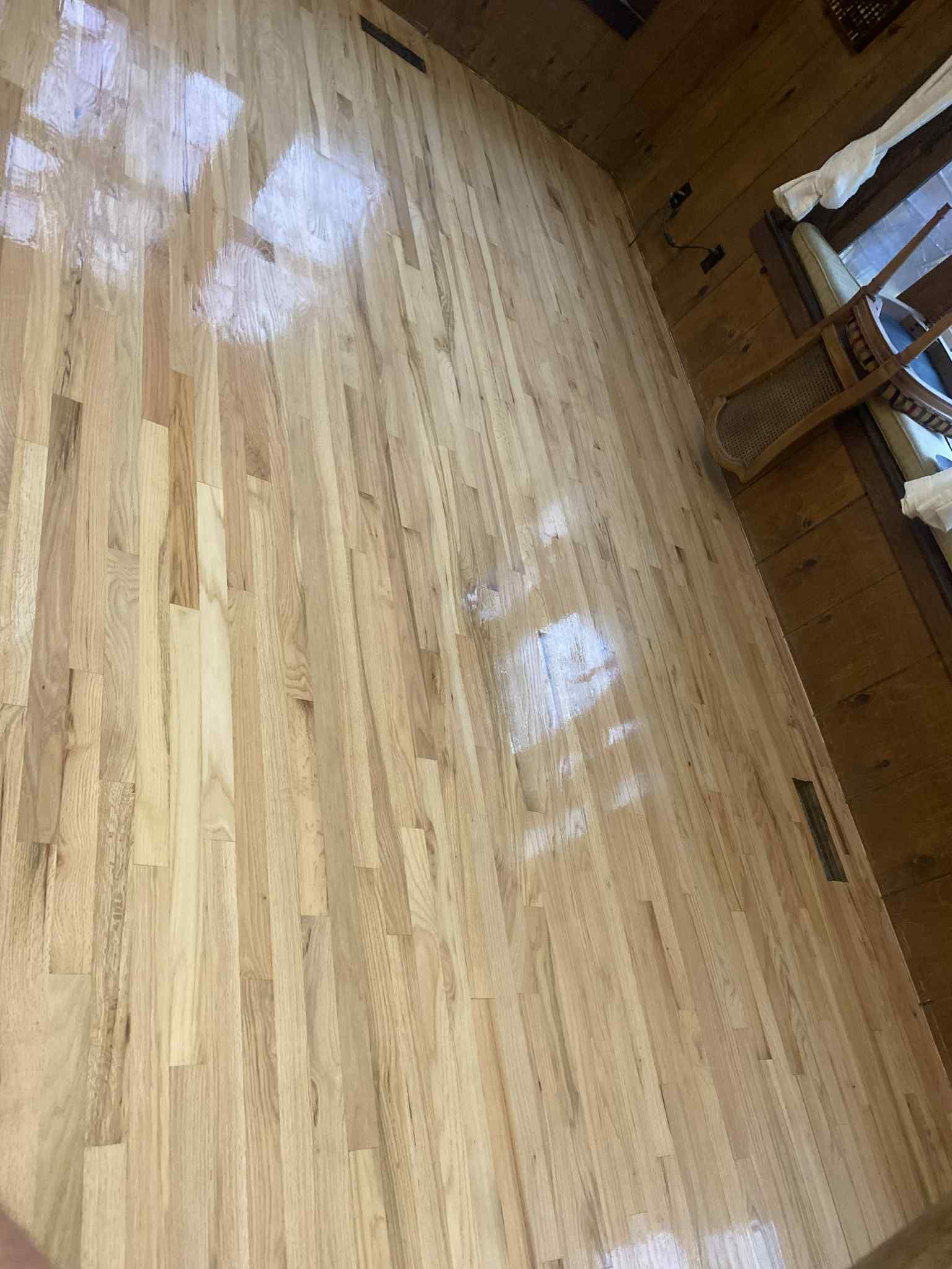Light-colored hardwood floor with some shine, likely recently finished. In a room with wood paneling and a window.