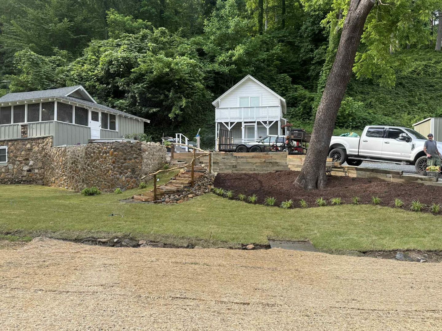 Buildings near a tree, with a truck parked nearby. Green grass and trees frame the scene.