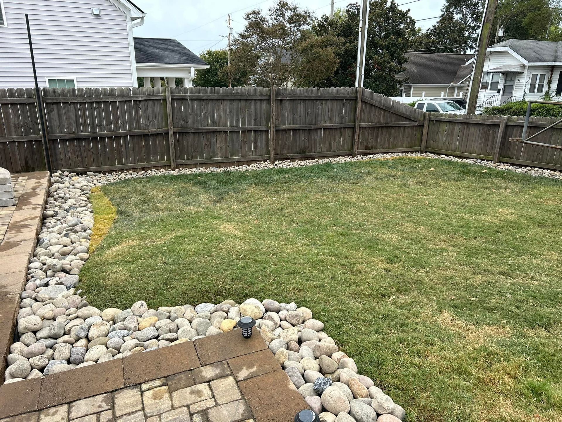 Backyard with a brown fence, rock border, and grass lawn.