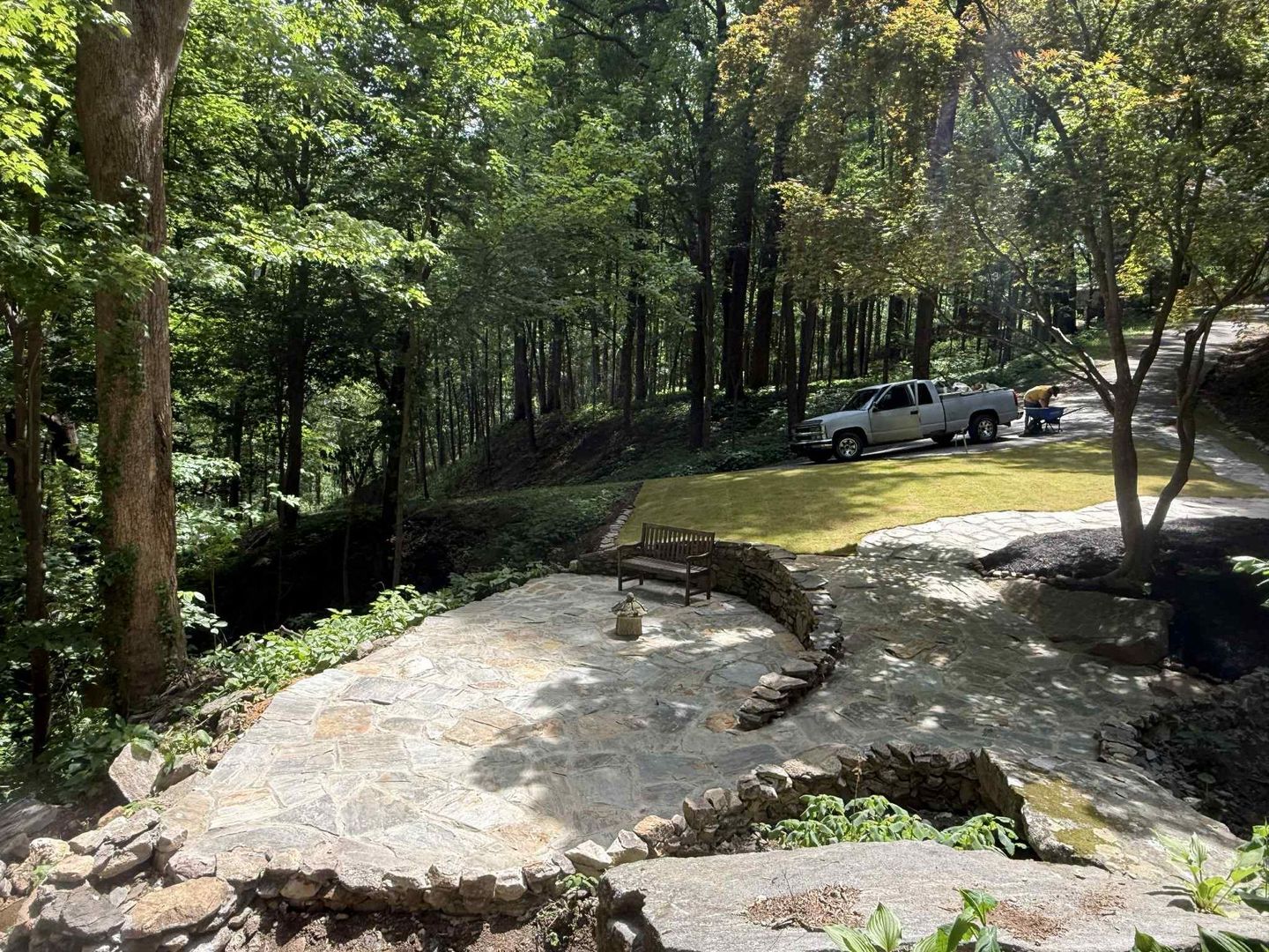 Stone patio overlooking a wooded area. A truck is parked on grass with trees in the background.