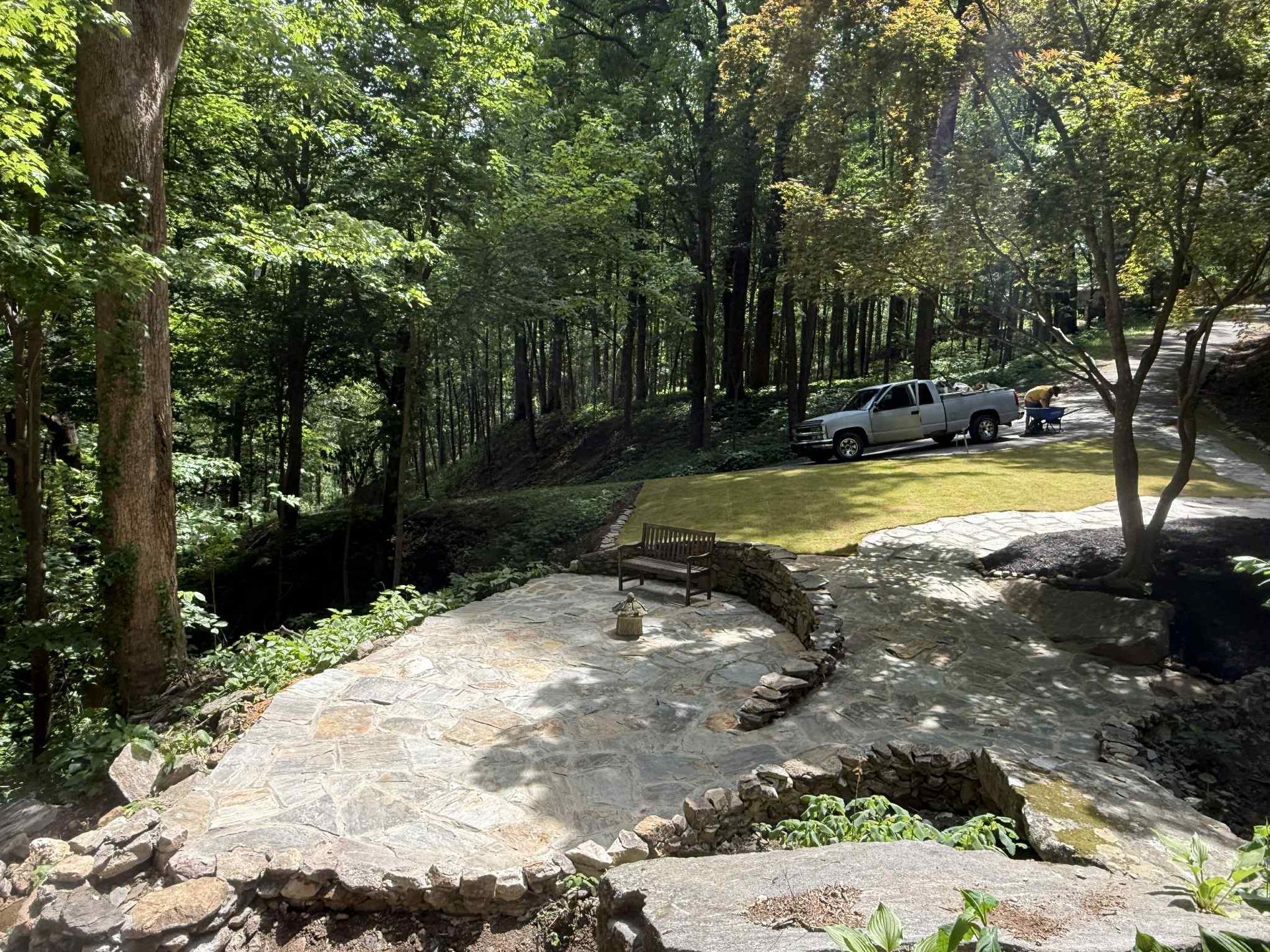 Stone patio overlooking a wooded area. A truck is parked on grass with trees in the background.