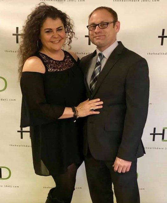 Woman in black dress and man in suit, smiling, posing together at an event.