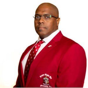 Man wearing glasses, red jacket, and tie, looking forward with serious expression.