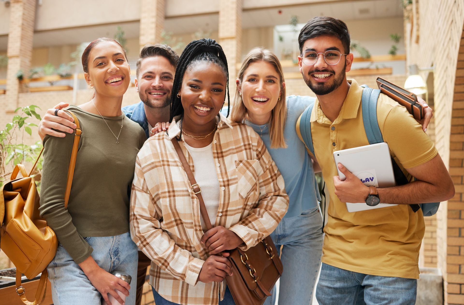 Group of students smiling, posing for a photo in a brick-walled university building.