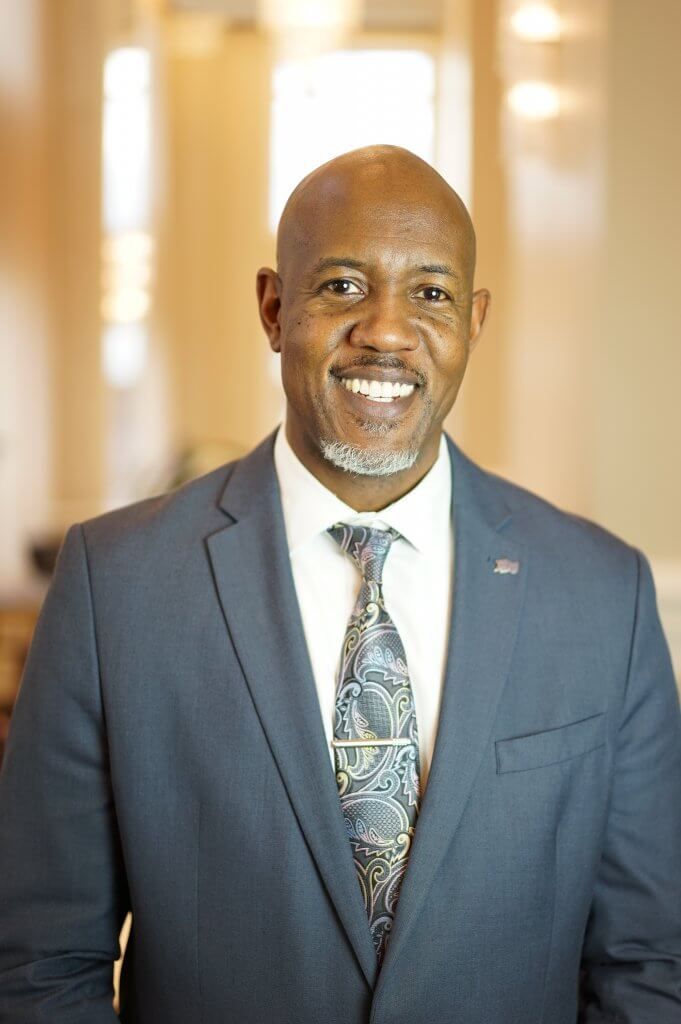Man in blue suit and paisley tie smiles, indoors.