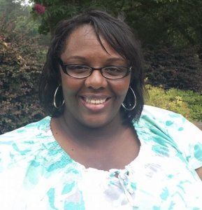 Woman with glasses and hoop earrings smiles outdoors wearing a patterned top. Woman with glasses and hoop earrings smiles outdoors wearing a patterned top.