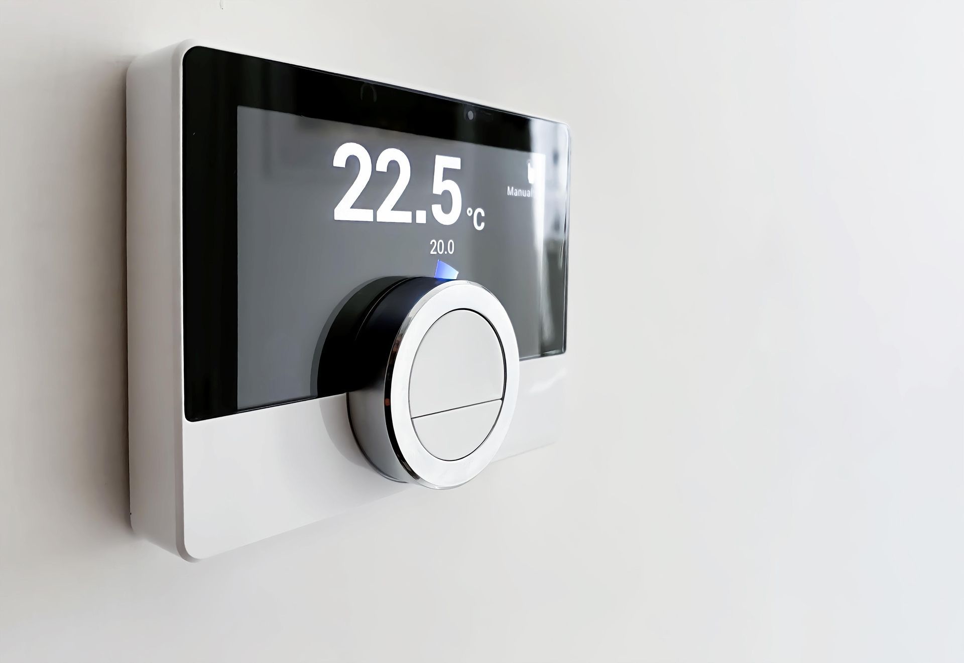 Smart thermostat on a white wall displaying 22.5°C. It has a black screen and a silver dial.