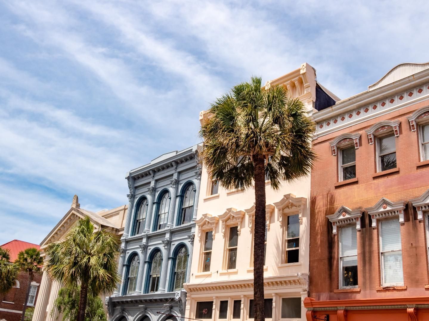 Row of historic buildings with palm trees against a blue sky.