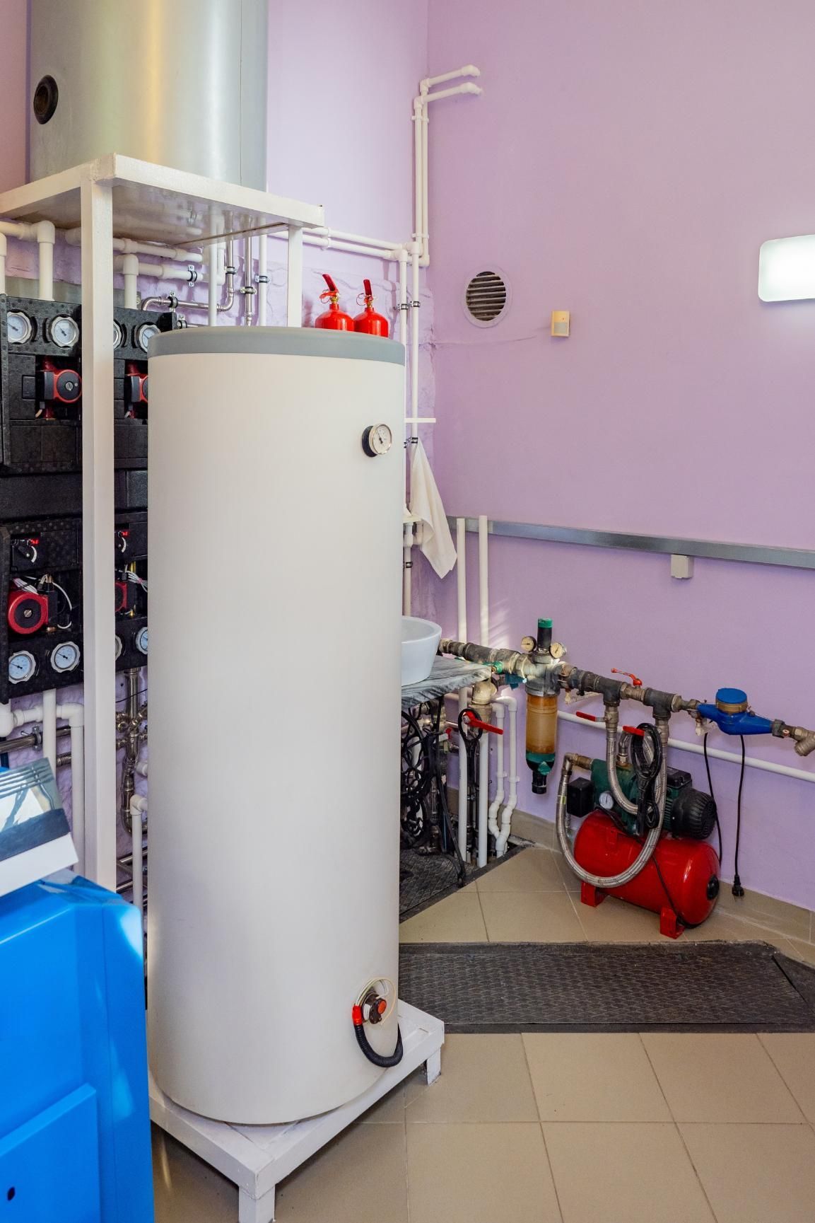 Water heater and related equipment in a utility room with purple walls and tiled floor.