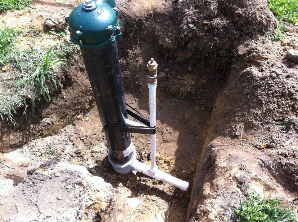 A black pipe is sitting in the dirt next to a white pipe.