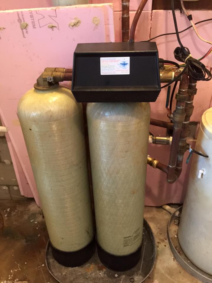 A water filter is sitting in a basement next to a water heater.