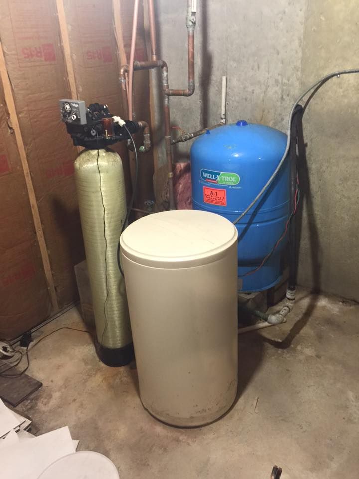 A blue water tank is sitting next to a white tank in a basement.