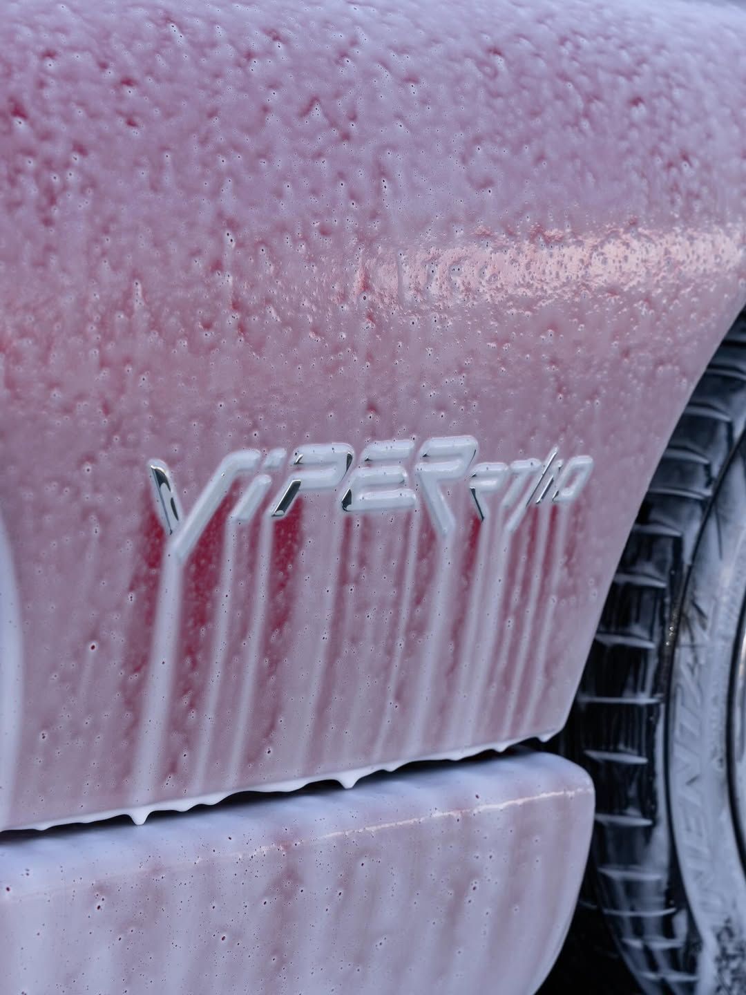 Close-up of a red Dodge Viper car panel covered in thick, white soap suds, highlighting the Viper SRT10 emblem.