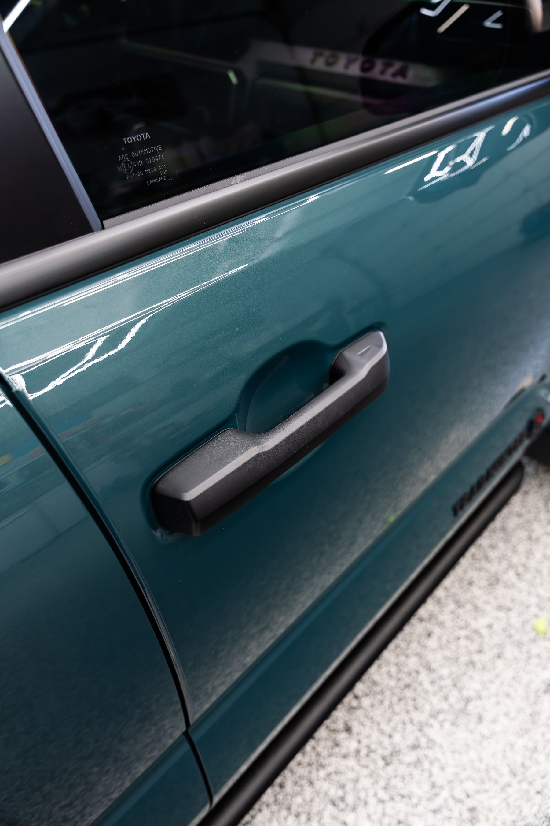 A teal green car door featuring a black handle, with a partial view of the window and trim.